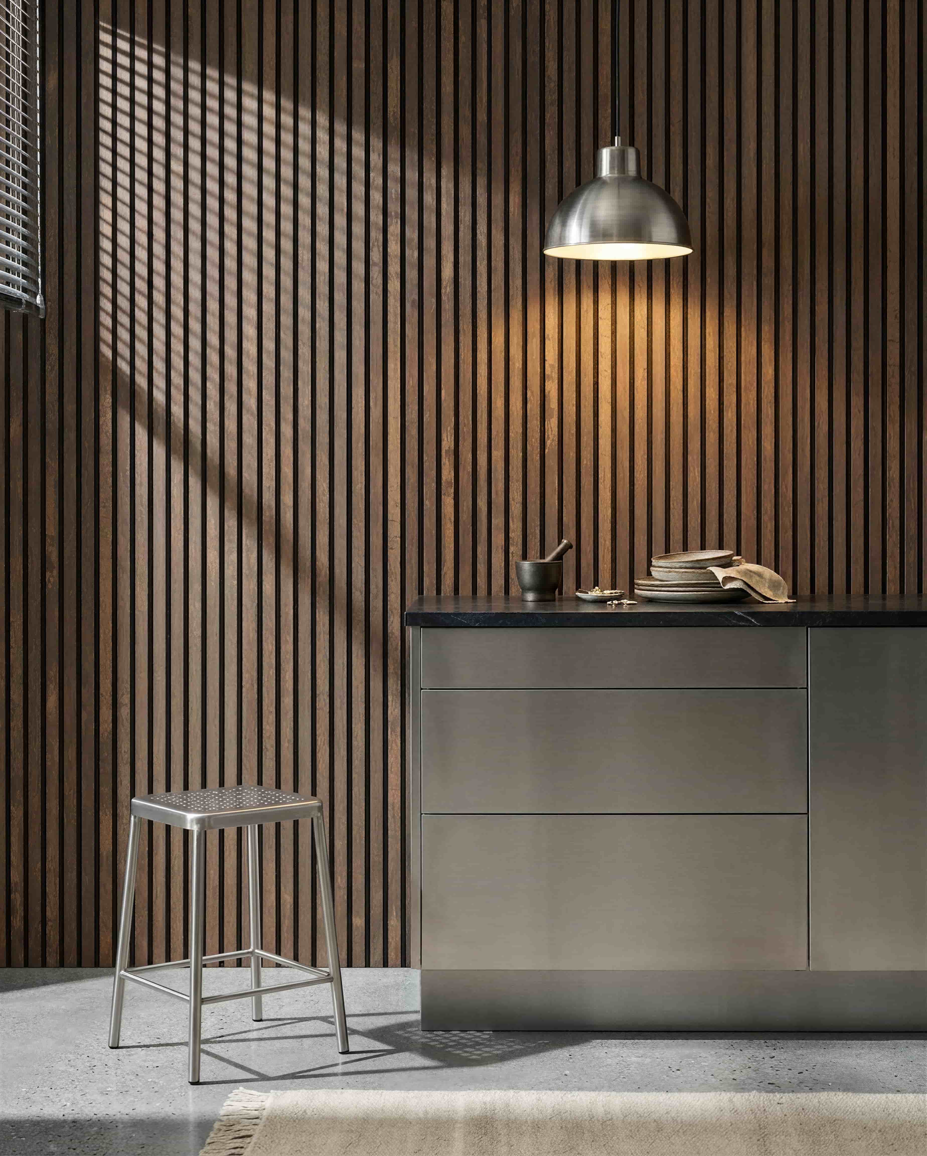 Cuisine avec un mur acoustique à lattes WoodUpp Akupanel Oxide Copper, un plan de travail en acier inoxydable, un tabouret en métal, une suspension, de la vaisselle assortie, et un mortier et pilon.