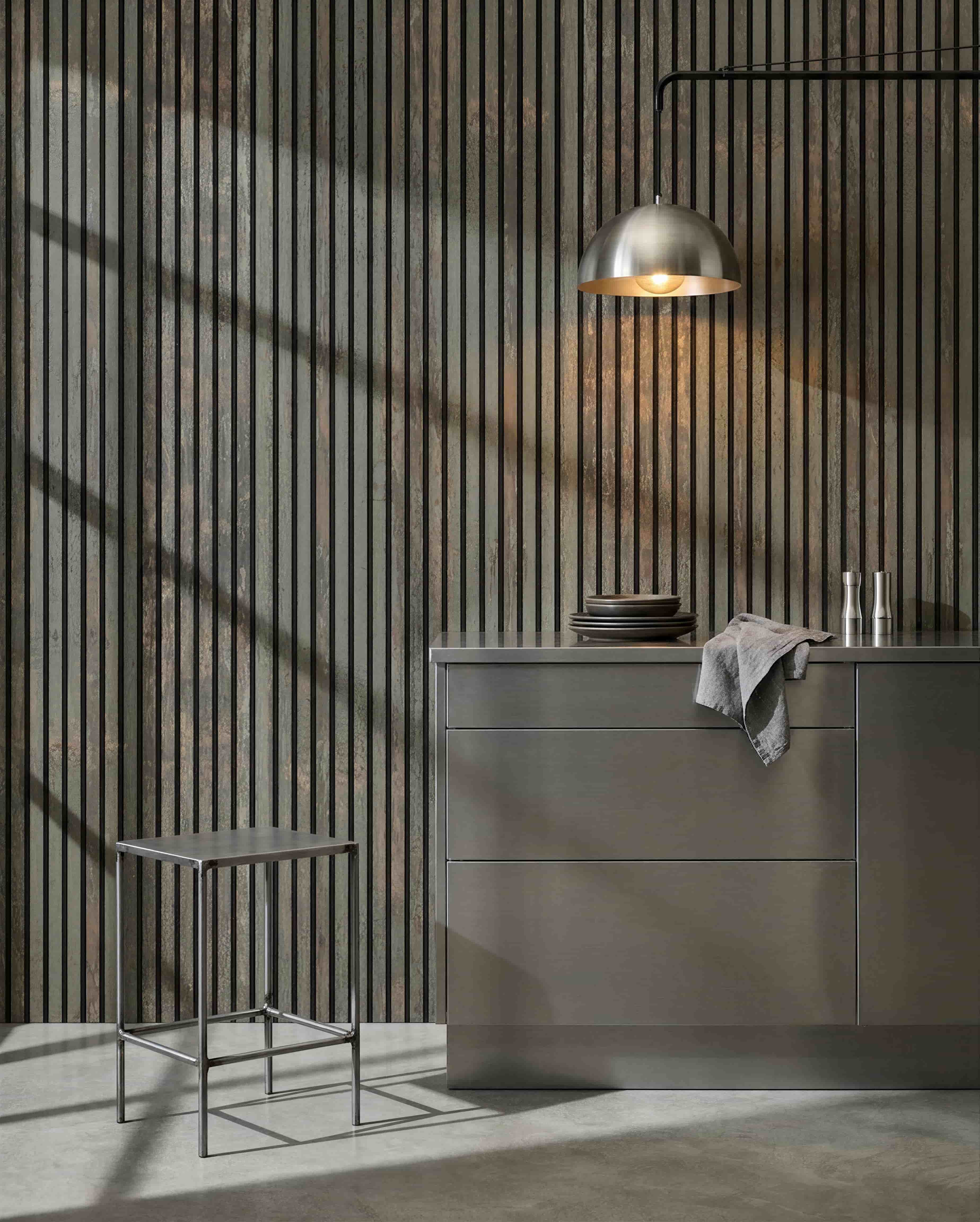 Cuisine minimaliste avec tabouret en métal, îlot grey et vaisselle, mettant en scène un panneau acoustique en bois WoodUpp Akupanel en Oxide Grey/Black Felt pour le contrôle du son.