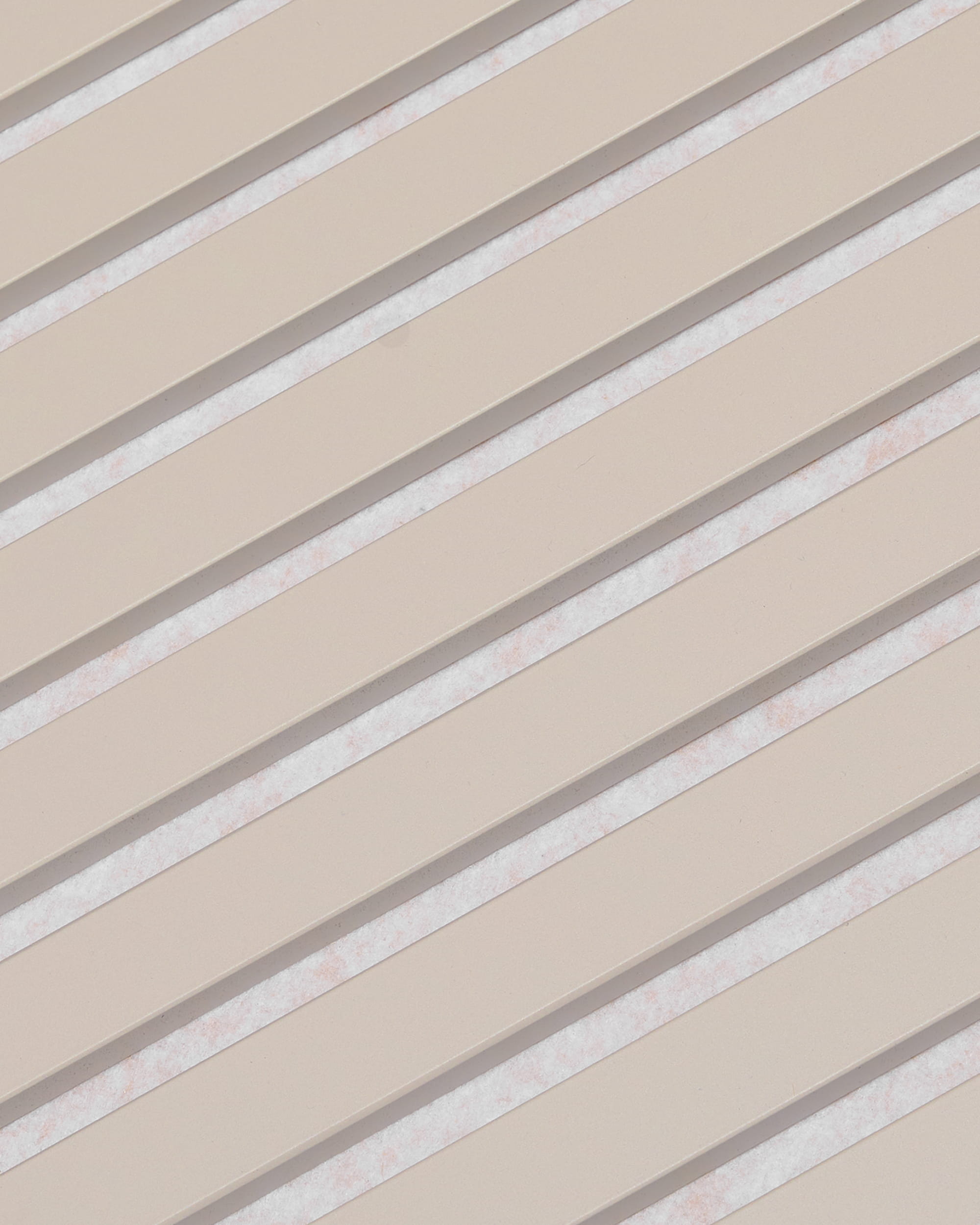 Des lamelles beiges disposées en diagonale, entrecoupées despaces blancs, forment un motif rayé sur le panneau acoustique WoodUpp Akupanel, finition feutre « Soft Linen Light Beige », 240 x 60 cm.