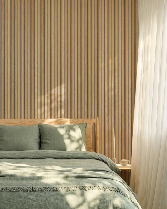 Chambre nordique minimaliste avec un mur WoodUpp Akupanel en chêne Panneau acoustique, une literie vert sauge, un cadre de lit en bois et des rideaux blancs voilés.