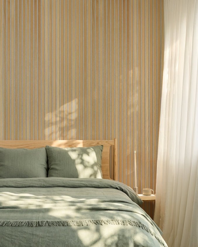 Chambre nordique minimaliste avec linge de lit vert sauge et un panneau acoustique à lattes WoodUpp Classic Oak Akupanel ; la lumière du soleil crée de douces ombres sur le lit.