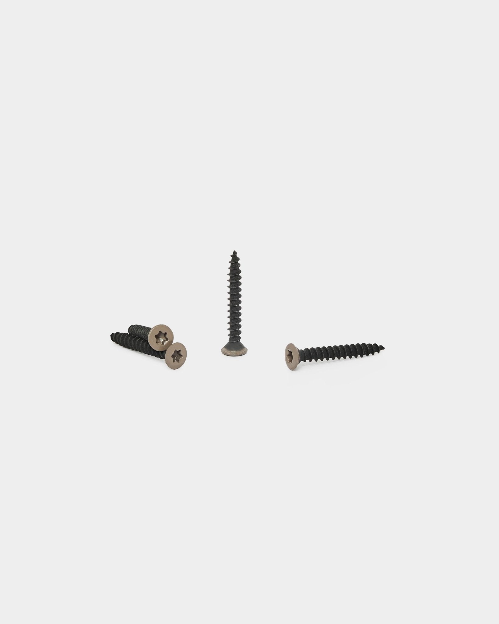 Trois vis warm grey pour panneaux acoustiques WoodUpp sont disposées sur un fond blanc, l’une debout et deux à plat, avec les têtes visibles.