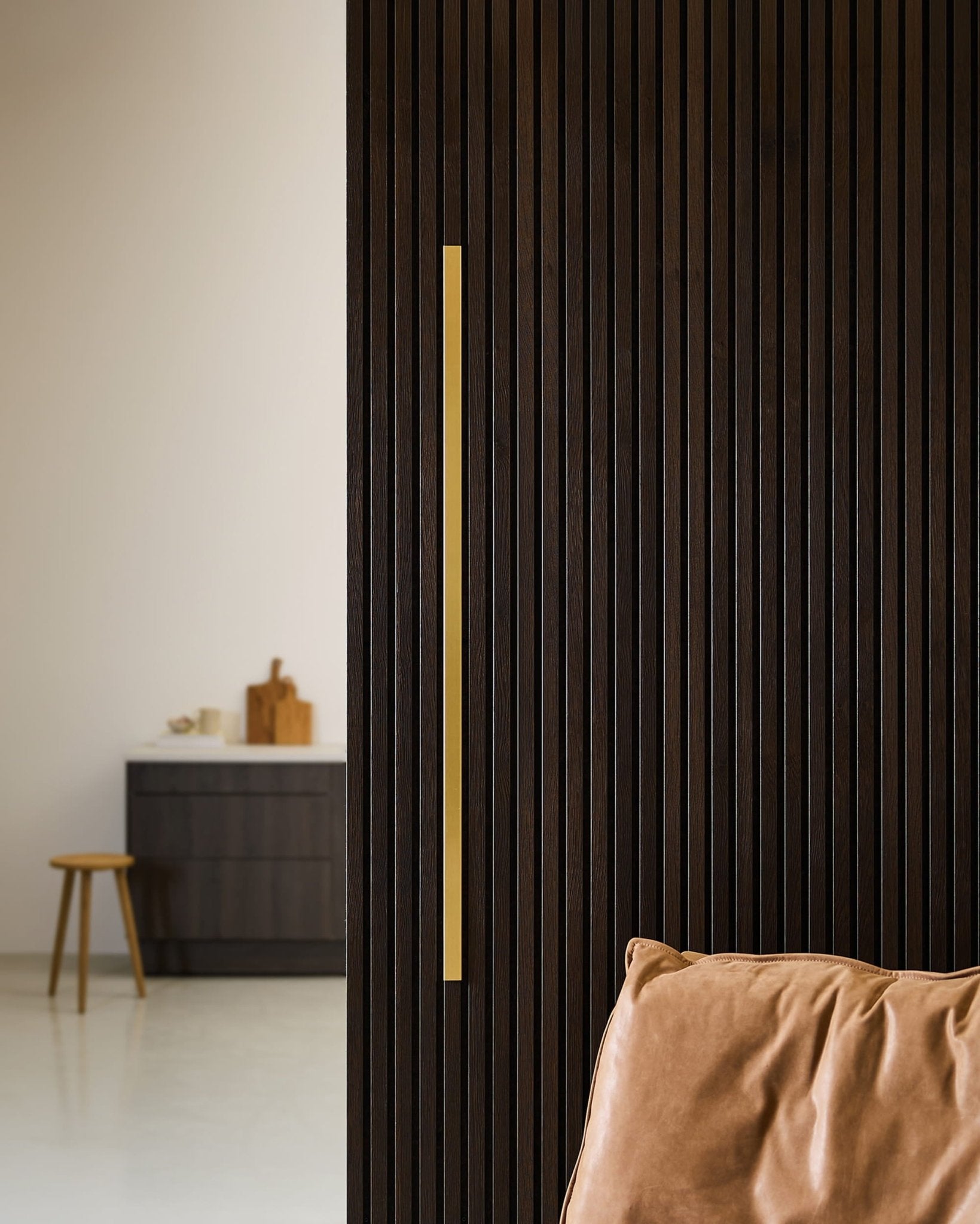 Intérieur nordique minimaliste avec un panneau acoustique WoodUpp Liva couleur laiton de 120 cm, une poignée dorée, un fauteuil en cuir beige et une décoration épurée.