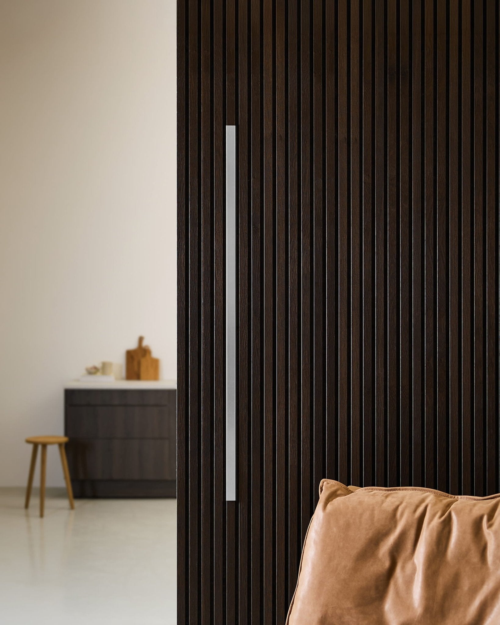 Porte Akupanel en bois foncé avec revêtement WoodUpp Liva, poignée en acier de 120 cm, moulures décoratives, coussin en cuir et cuisine nordique minimaliste avec tabouret.
