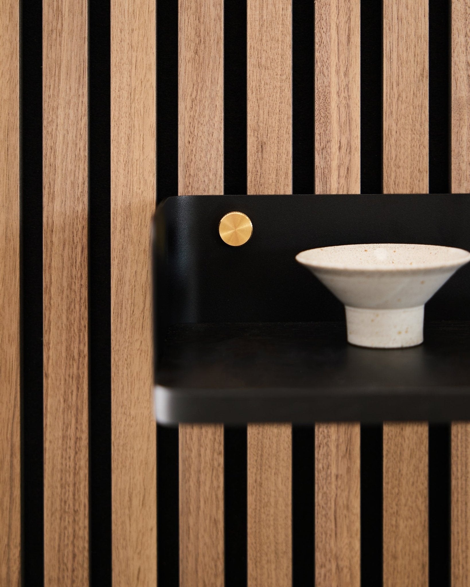 Bol en céramique posé sur l’étagère Linn de WoodUpp, 39,9 cm en black oak avec des lattes vertical black et une touche brass, dans un esprit minimaliste nordique.