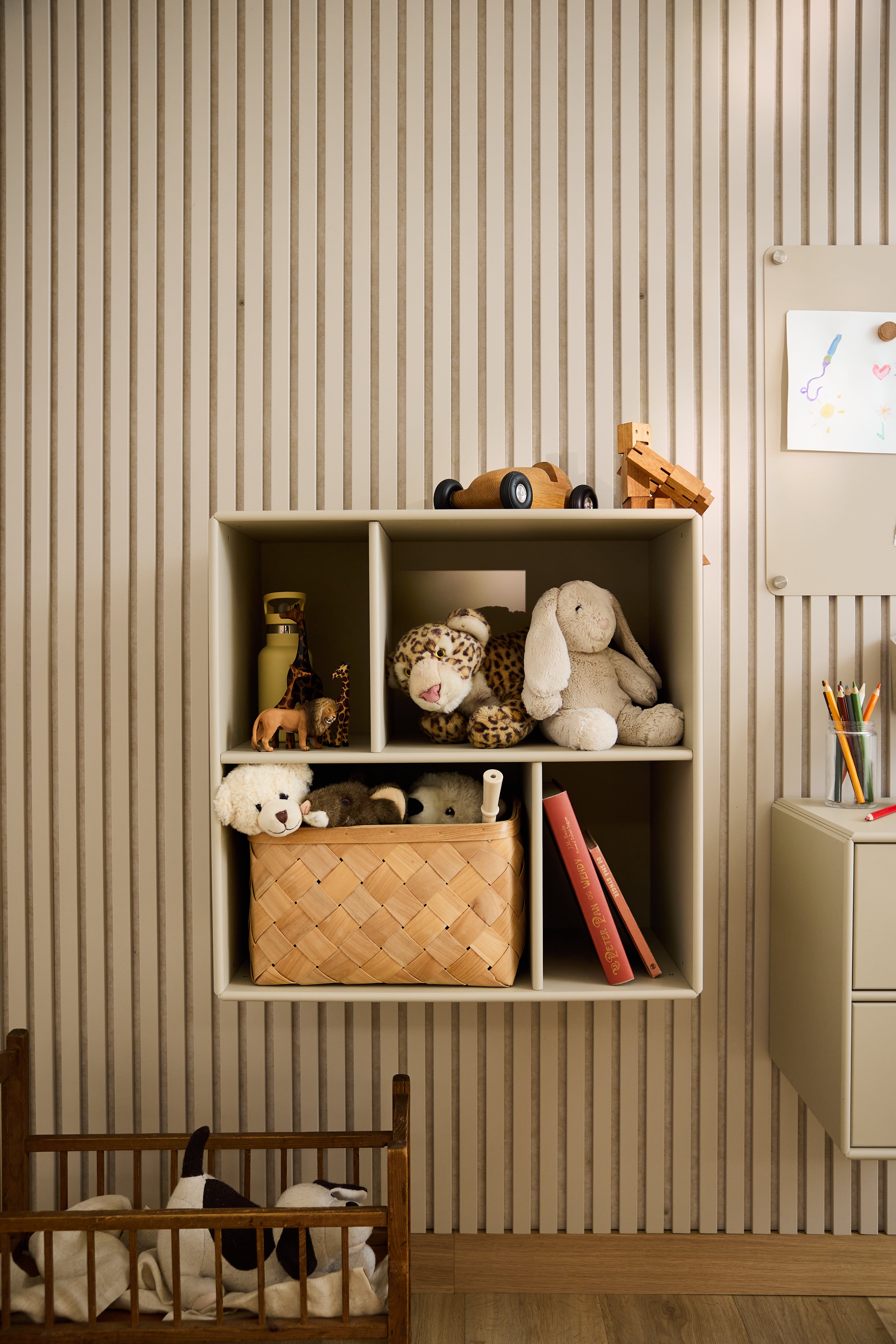 Larmoire ouverte WoodUpp Arka, de couleur beige, remplie de jouets et de livres, se détache sur le fond dun papier peint rayé dans une chambre denfant, illustrant ainsi le design nordique minimaliste.