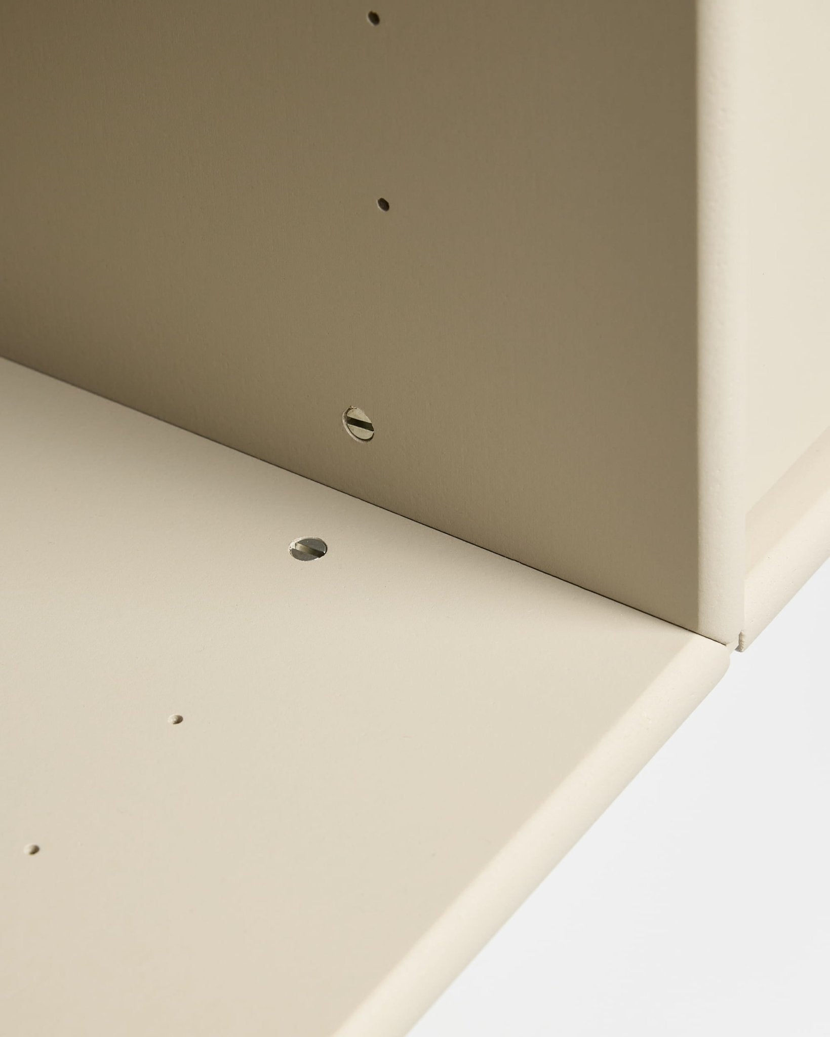 Gros plan sur deux panneaux beige de la console TV « Arka » de WoodUpp, assemblés à angle droit et dotés de trous pré-percés pour un montage modulaire et le passage des câbles.