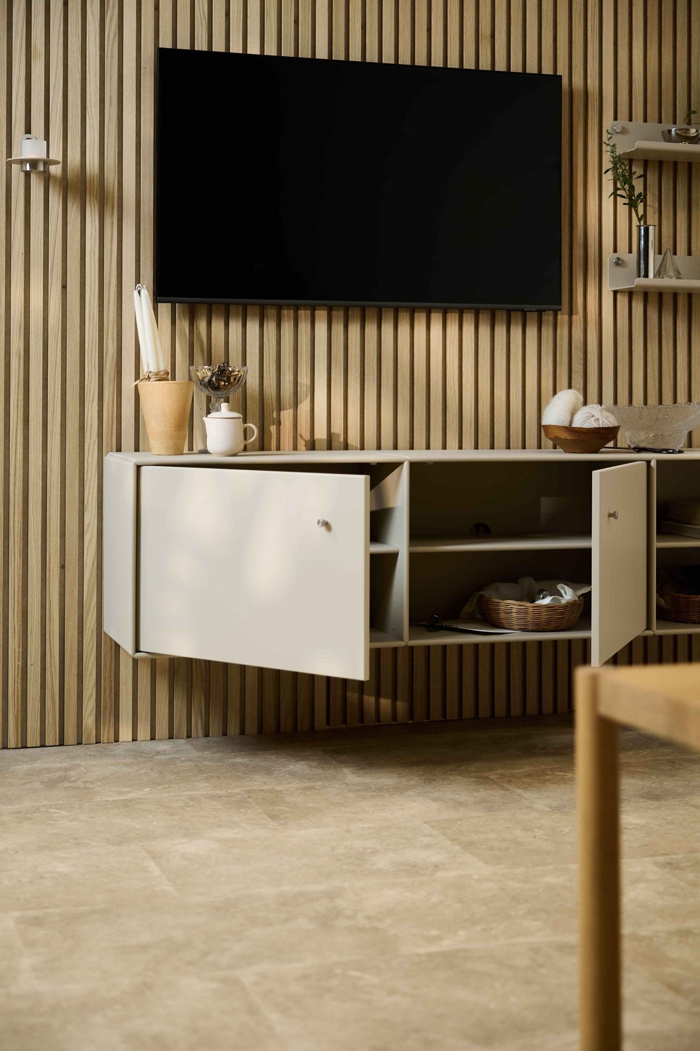 Salon moderne mettant en valeur le meuble TV Arka de WoodUpp, couleur beige, placé sous un meuble de rangement et un téléviseur, devant un mur acoustique en lattes de bois « Akupanel » de style nordique. Mobilier modulaire.