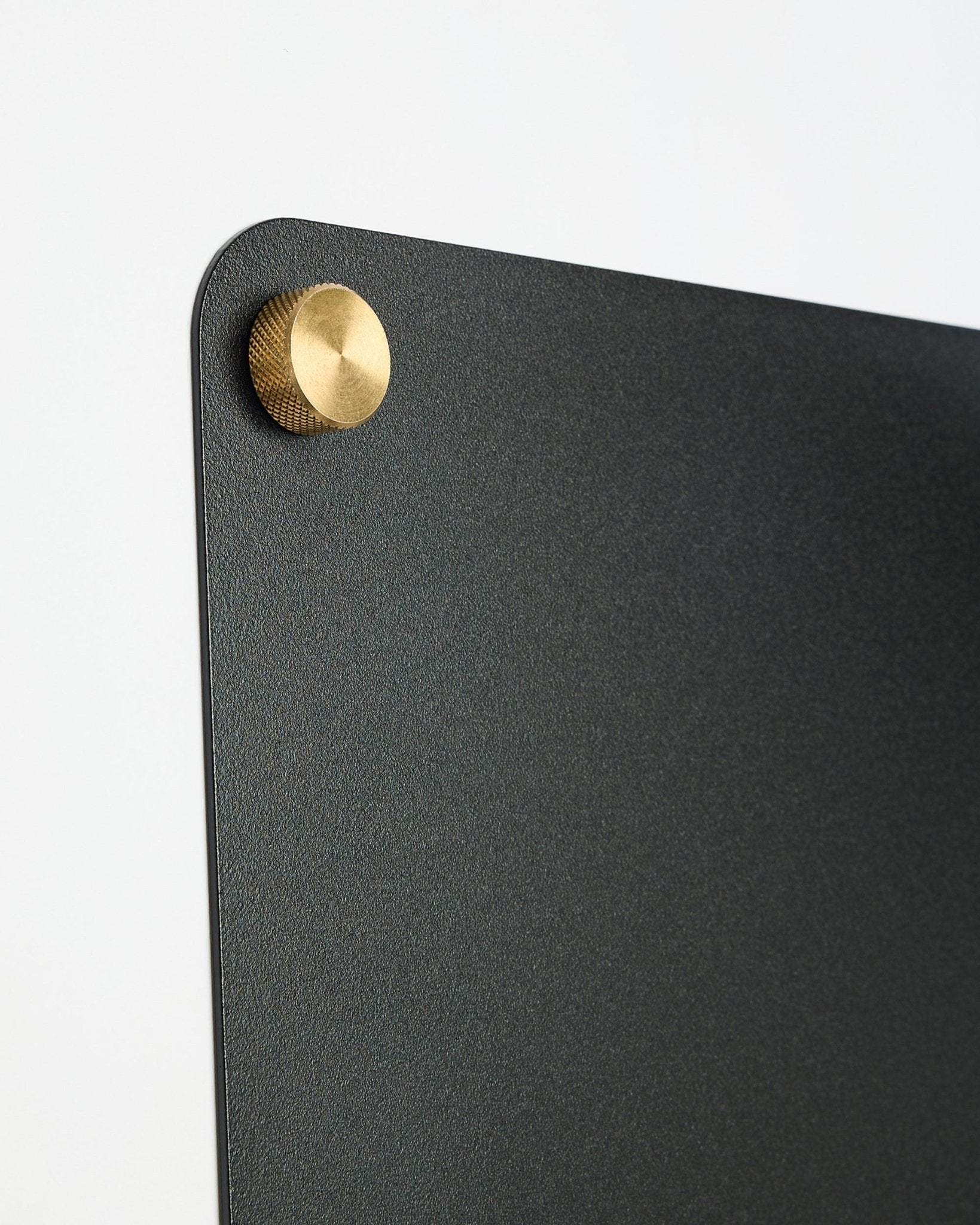 Gros plan sur un large black Norr tableau magnétique de WoodUpp, issu de la collection CREATE, avec une fixation en métal ronde colored dans le coin supérieur.