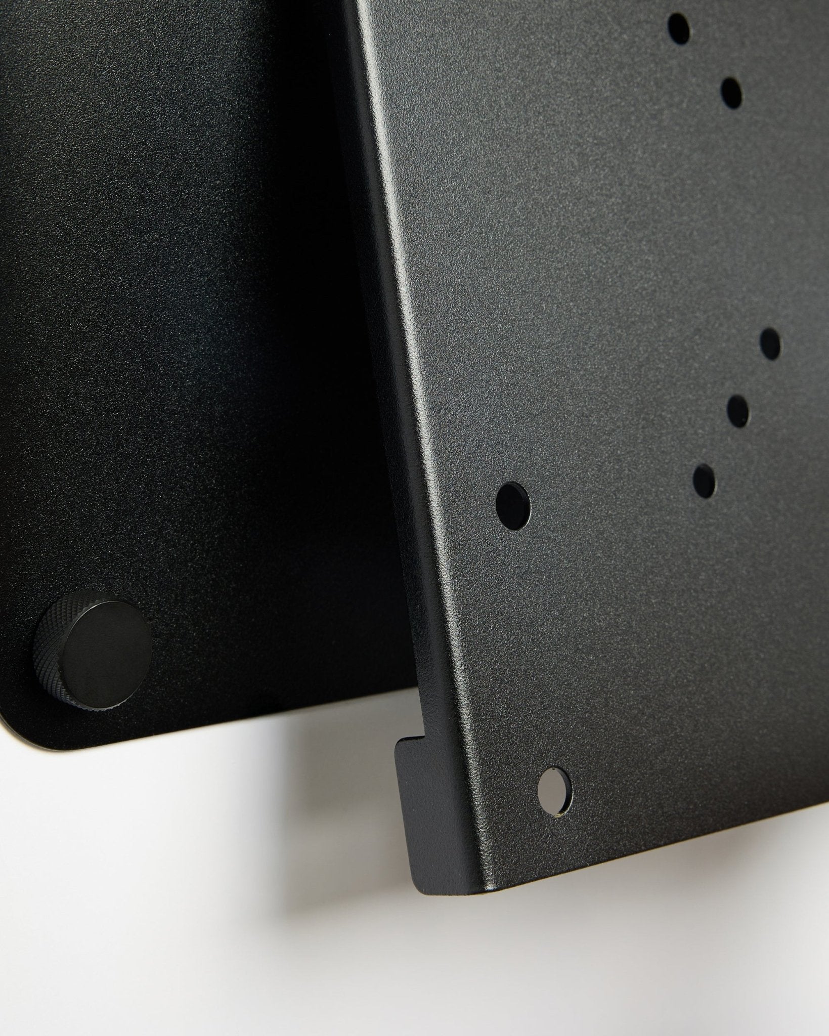 Gros plan sur le support TV Fjell (small) de WoodUpp, un support métallique black avec des trous circulaires et une molette de réglage, présenté sur fond blanc.