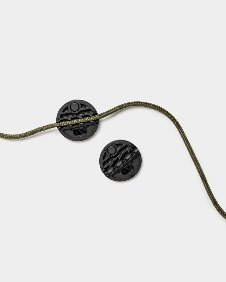 Deux bloque-cordons Gallery String Vindar de WoodUpp avec une corde tressée verte, présentés sur un fond uni gris clair.