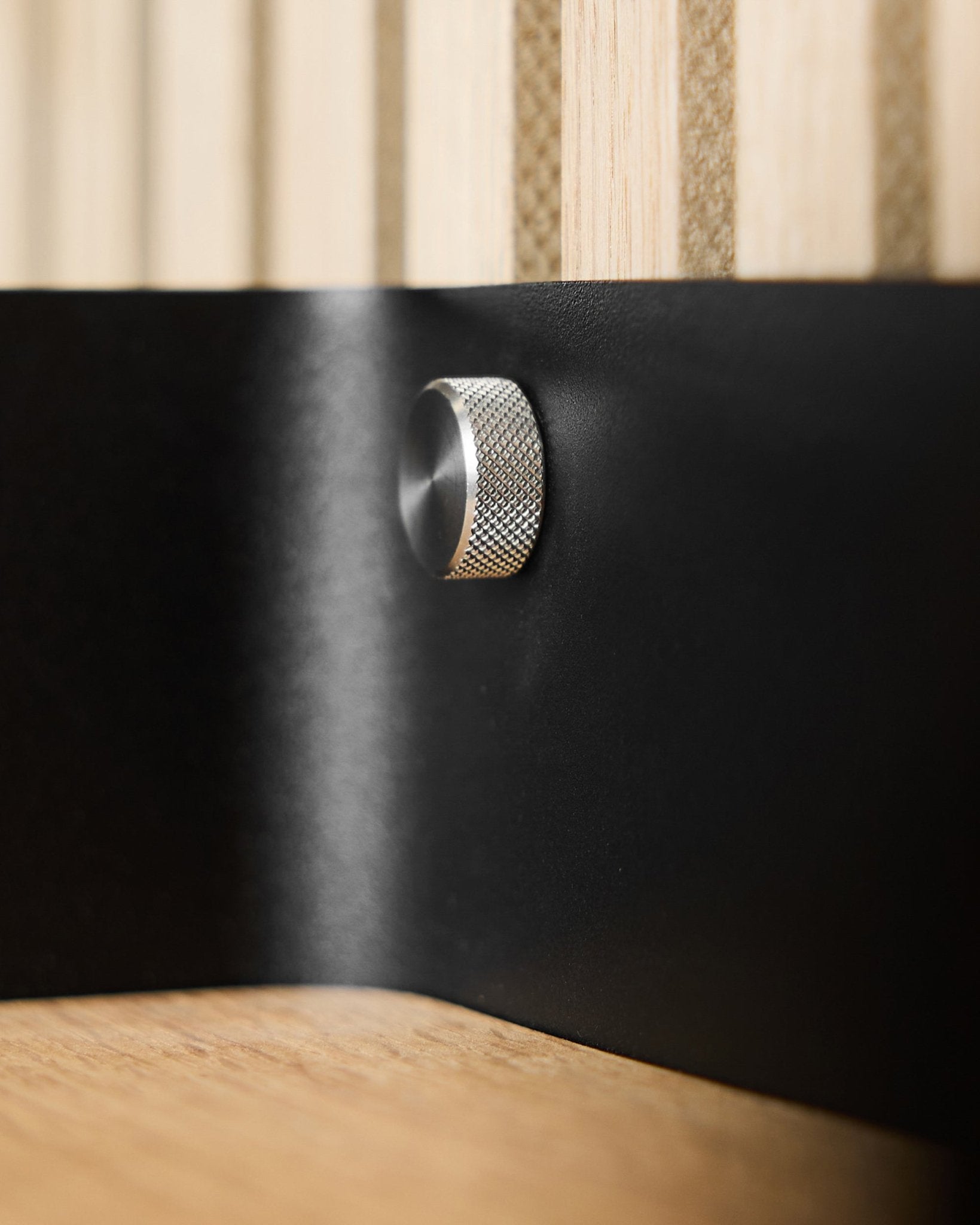 Gros plan sur deux vis moletées WoodUpp (M5x10 mm, acier inoxydable steel 20x8.8) sur une surface métallique black, avec des lattes acoustiques en bois Akupanel en arrière-plan.