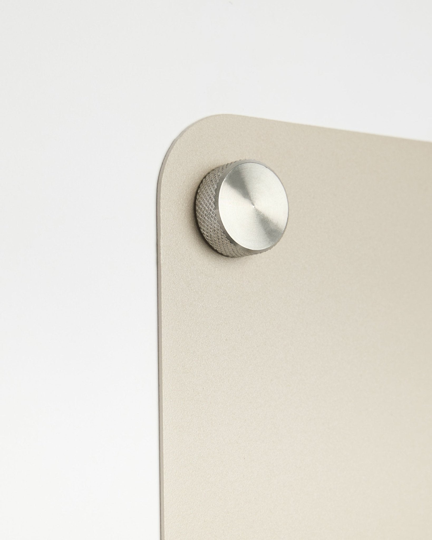 Gros plan sur un accessoire à bouton rond en métal fixé au tableau magnétique WoodUpp large beige Norr, avec un détail en verre dépoli sur fond blanc.
