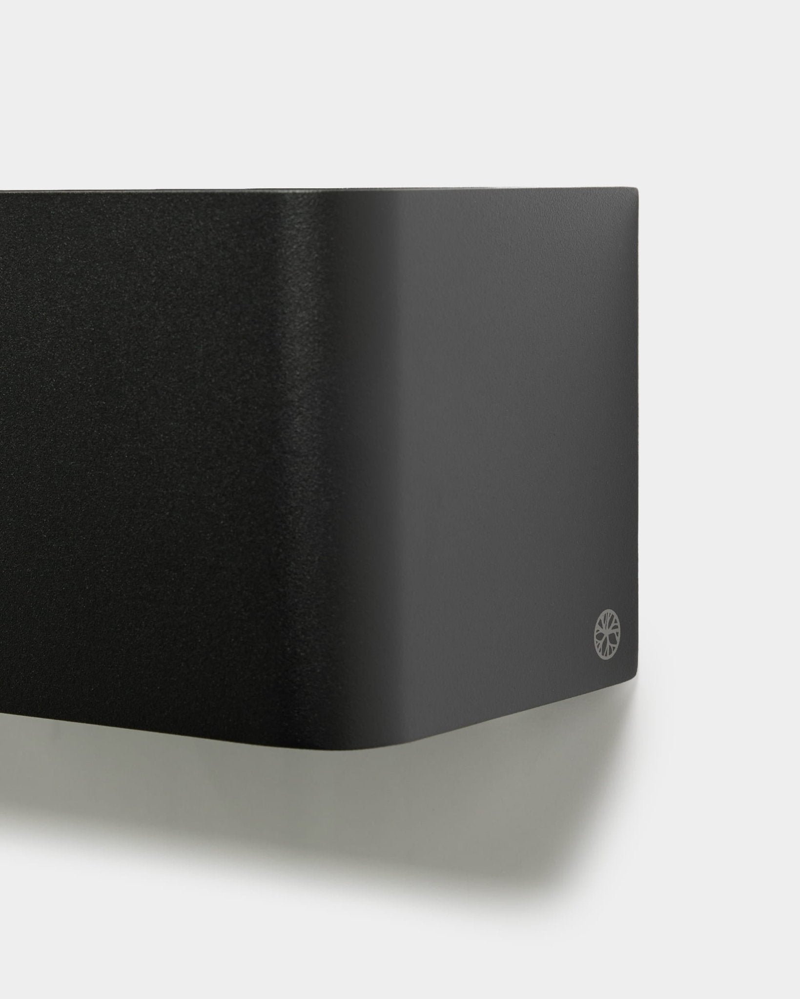 Gros plan sur le bac à plantes minimaliste WoodUpp Norr (23,9 cm, black) aux bords arrondis et avec logo, monté sur un mur blanc. Design d’accessoire acoustique nordique.