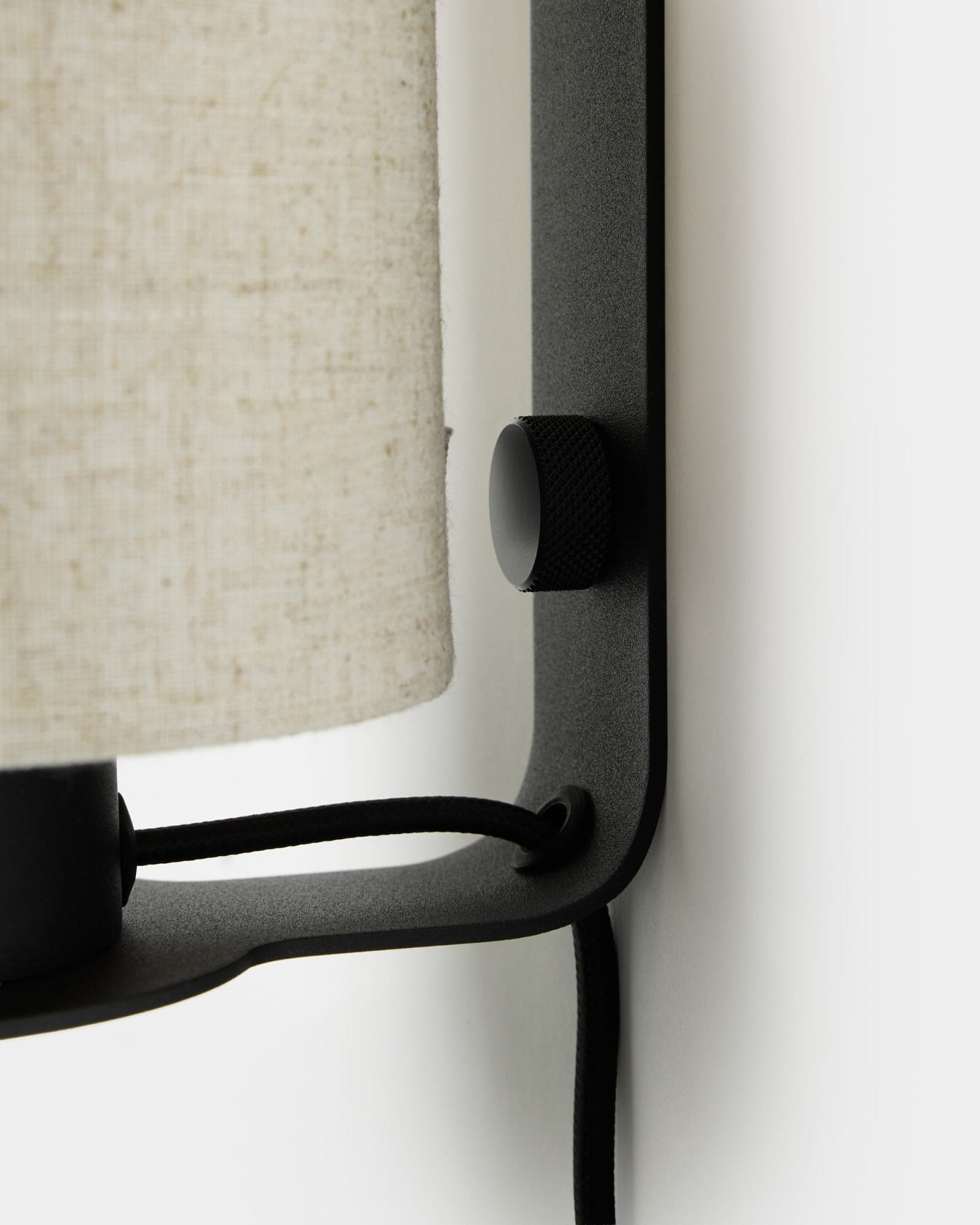 Gros plan sur l’applique murale Feya de WoodUpp en black et beige, avec bouton texturé, abat-jour en lin-coton et cordon visible, fixée sur un mur blanc.