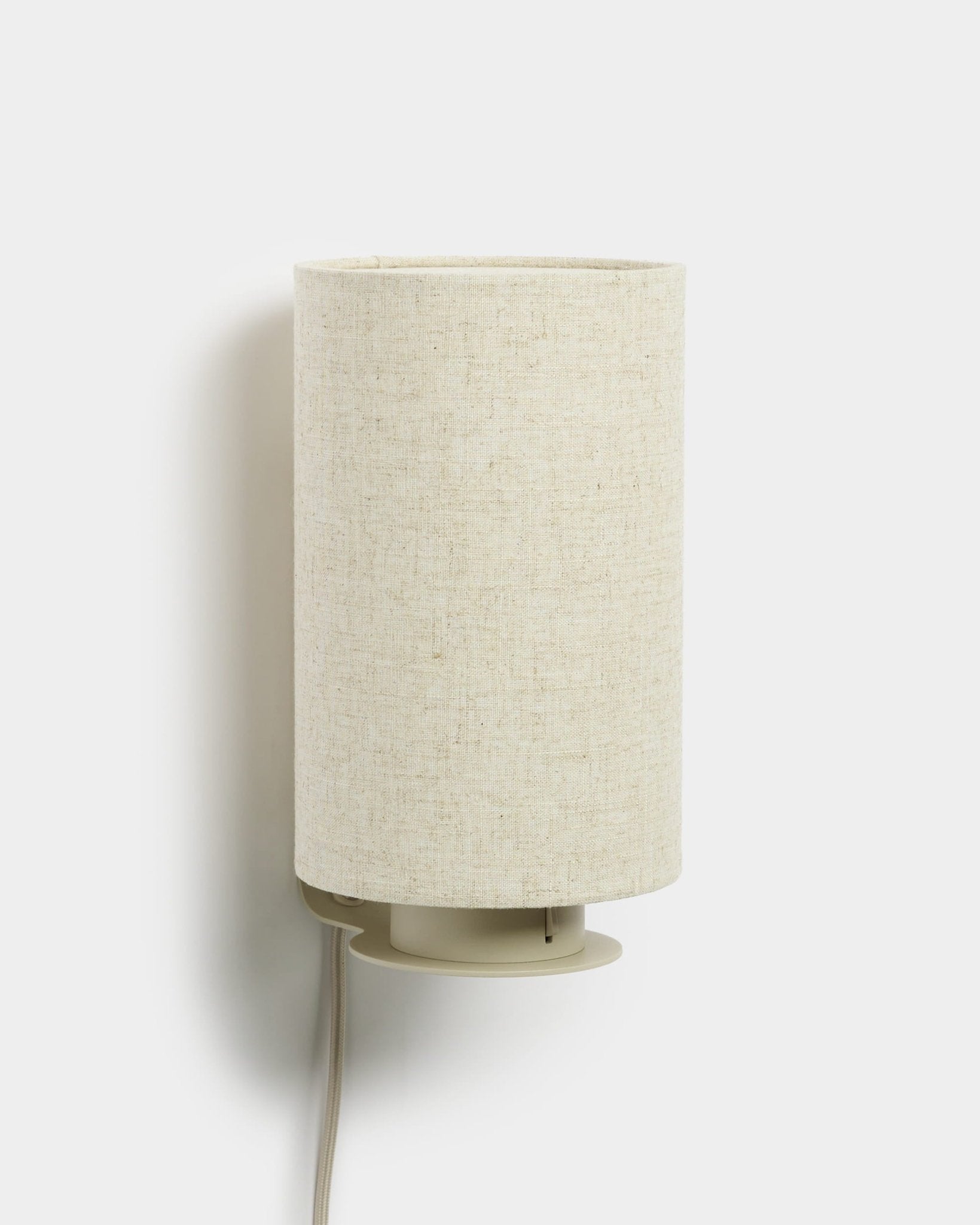 Feya | Wall Lamp par WoodUpp avec un abat-jour cylindrique en lin-coton et un cordon blanc apparent, finition beige, conçu pour s’accorder avec les panneaux acoustiques en bois.