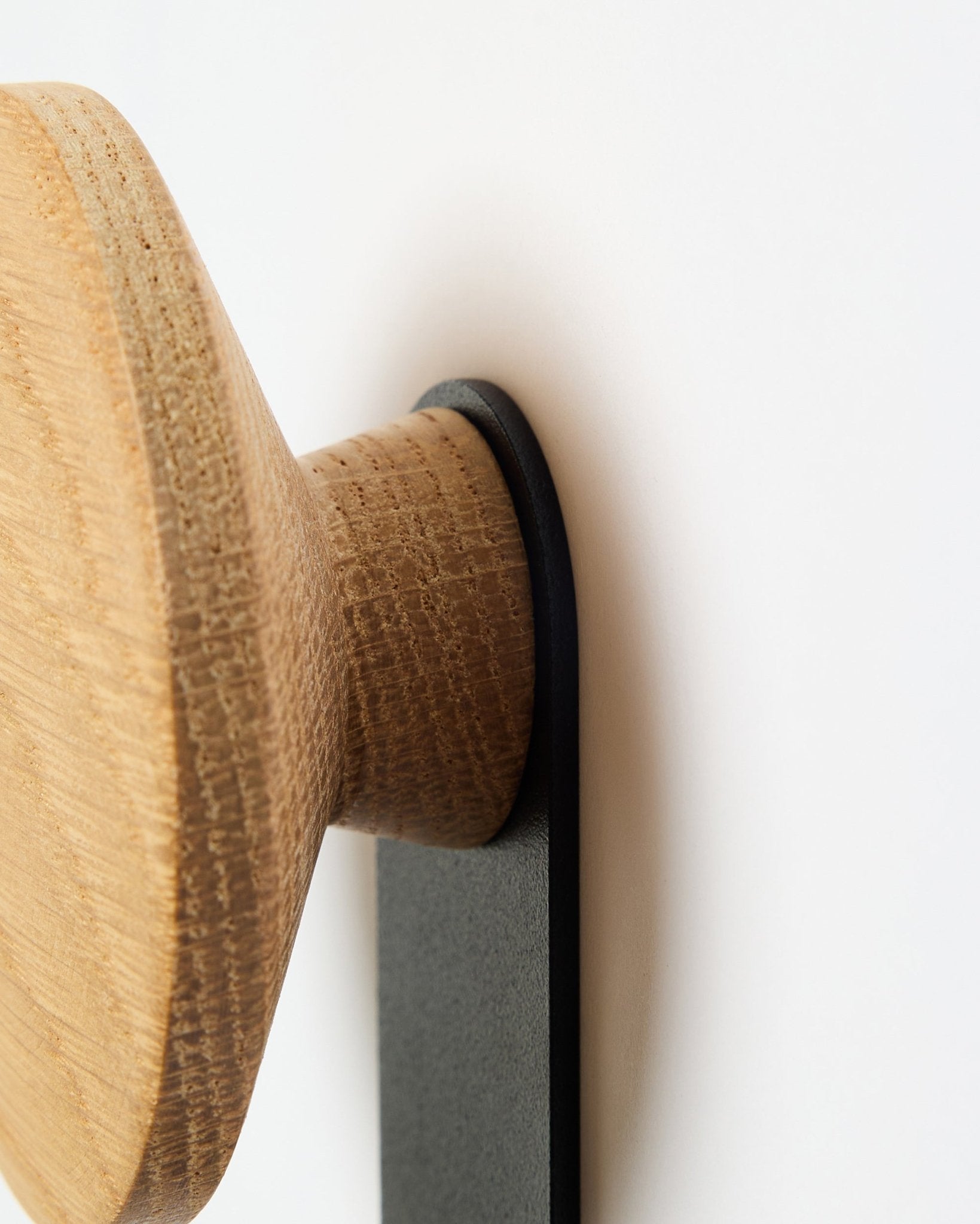 Gros plan sur le porte-manteau Linn Vertical en natural oak de WoodUpp, un accessoire avec bouton rond en bois monté sur un support black, conçu pour les panneaux acoustiques Akupanel.