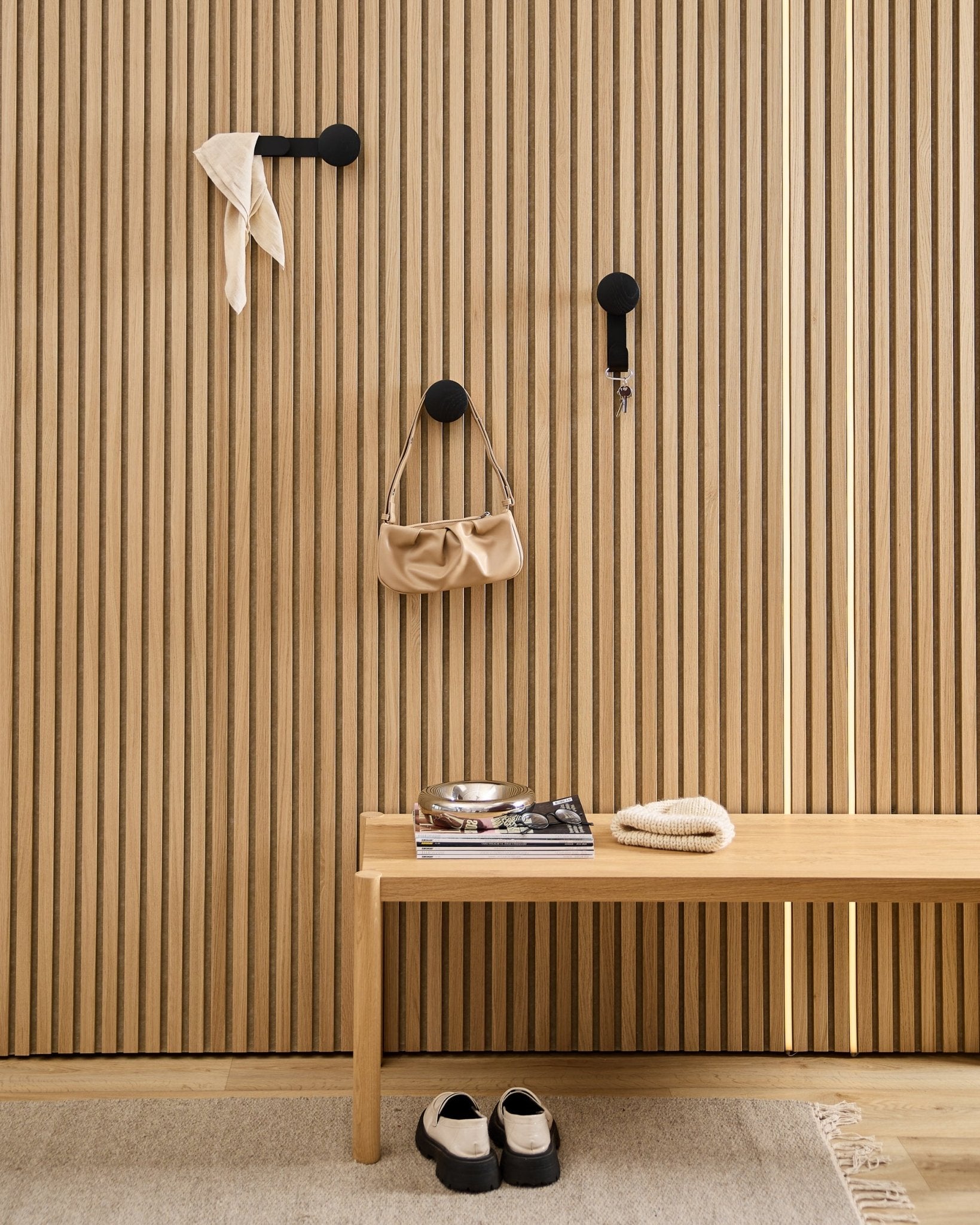 Entrée minimaliste avec un porte-manteau WoodUpp Linn Horizontal en Black Oak, avec des crochets black, un banc en bois, des chaussures, des livres et une coupelle. Style nordique.