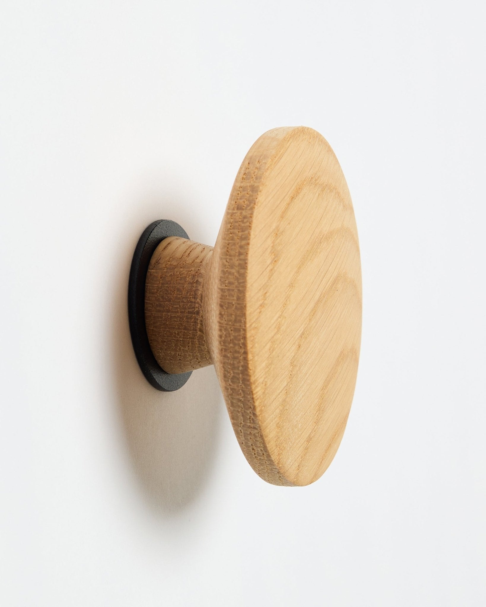 WoodUpp Linn I Single Hanger en natural oak, un crochet mural rond avec une base black, conçu comme accessoire à fixer sur des panneaux acoustiques en bois Akupanel.