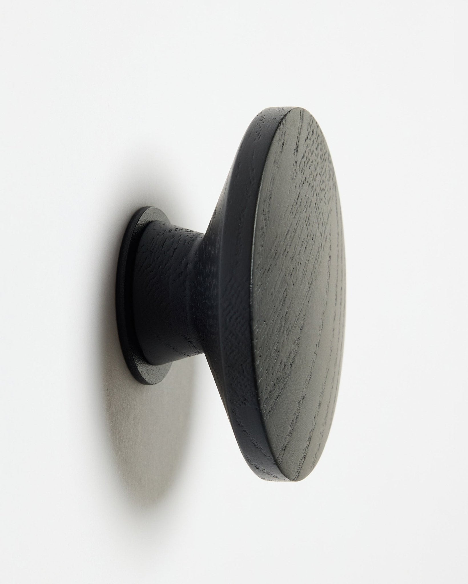 Un Linn | Single Hanger rond black oak de WoodUpp, conçu comme accessoire pour les panneaux acoustiques en bois Akupanel, fixé sur une surface blanche avec une légère ombre sur la gauche.