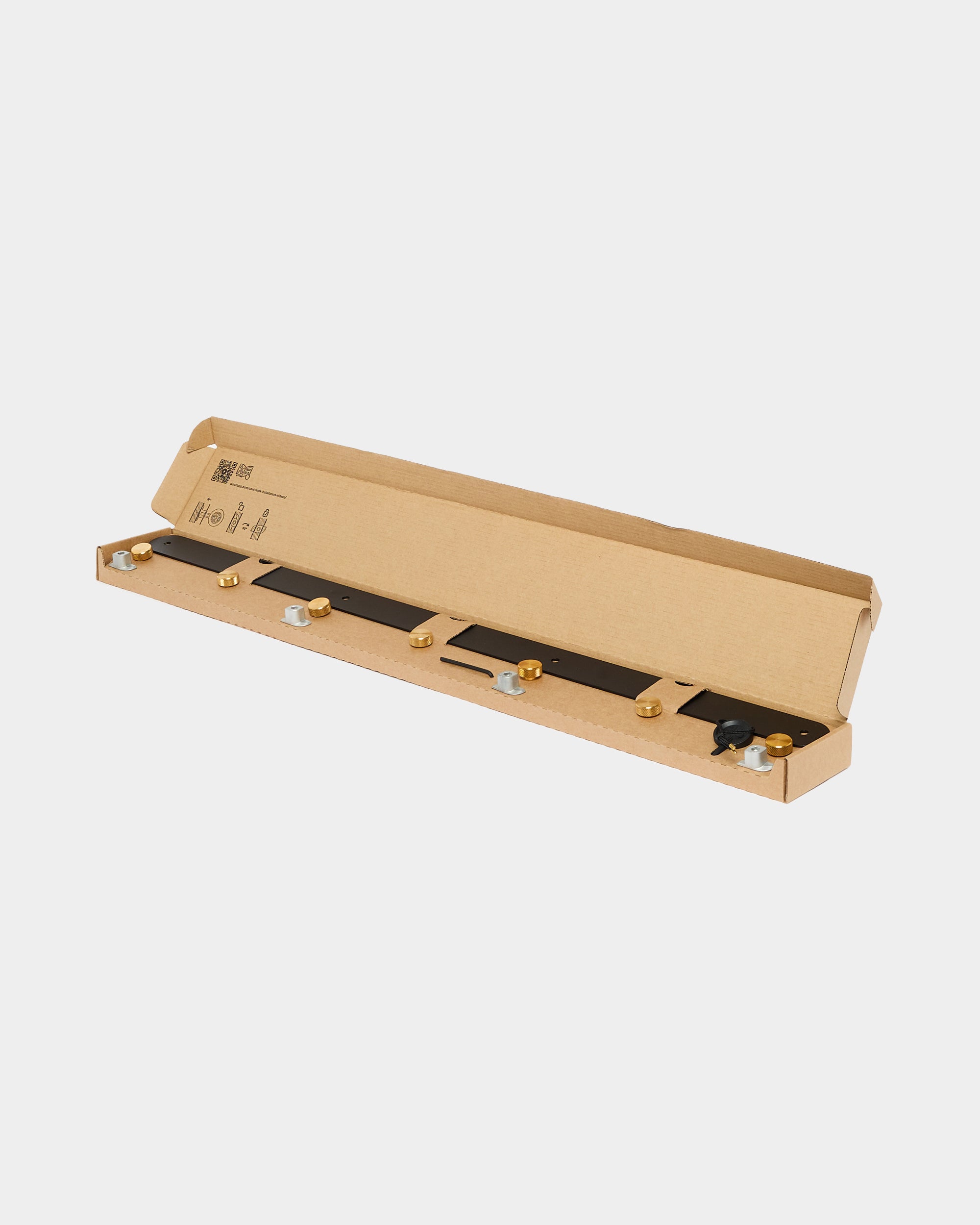 An open rectangular cardboard box displaying a black Akupanel installation strip with multiple gold and silver mounting components inside.