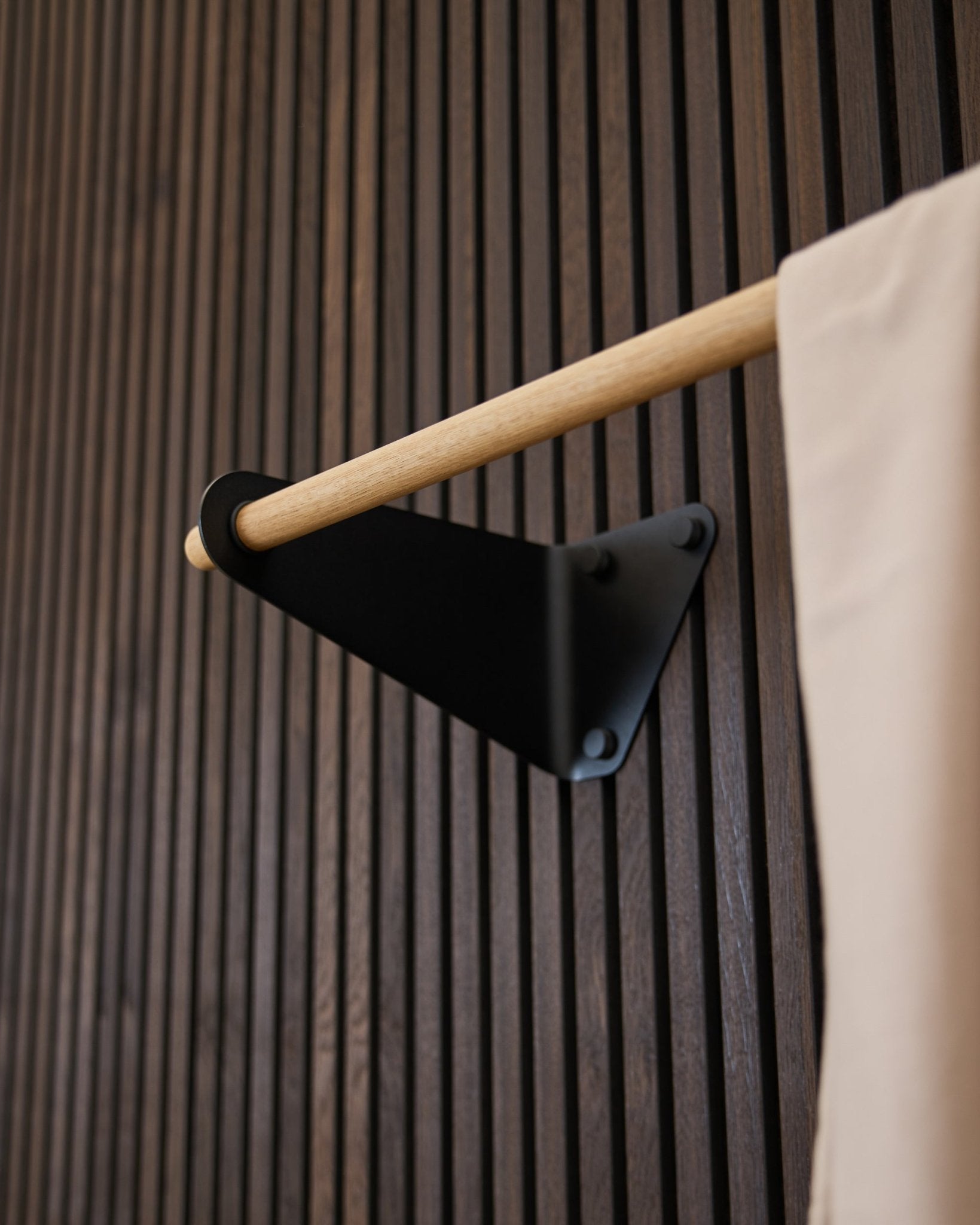 Patère Linn par WoodUpp en black (115,9 cm), montée sur un Akupanel rainuré foncé Panneau acoustique, avec un accent en tissu beige et un support black.