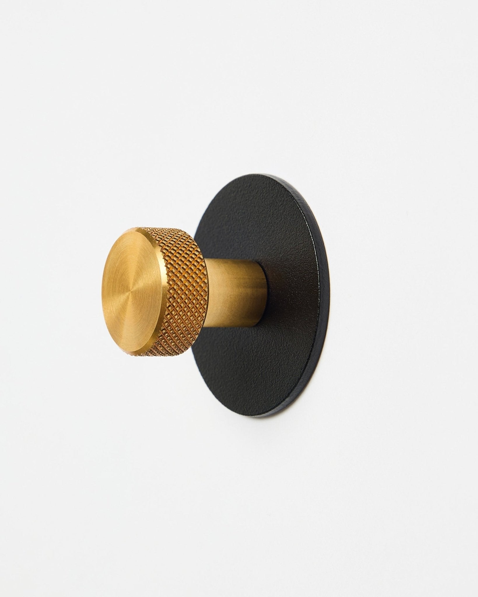Patère X1 Norr de WoodUpp avec bouton texturé brass et base black en steel thermolaqué, accessoire pour Akupanel, présentée sur fond blanc.