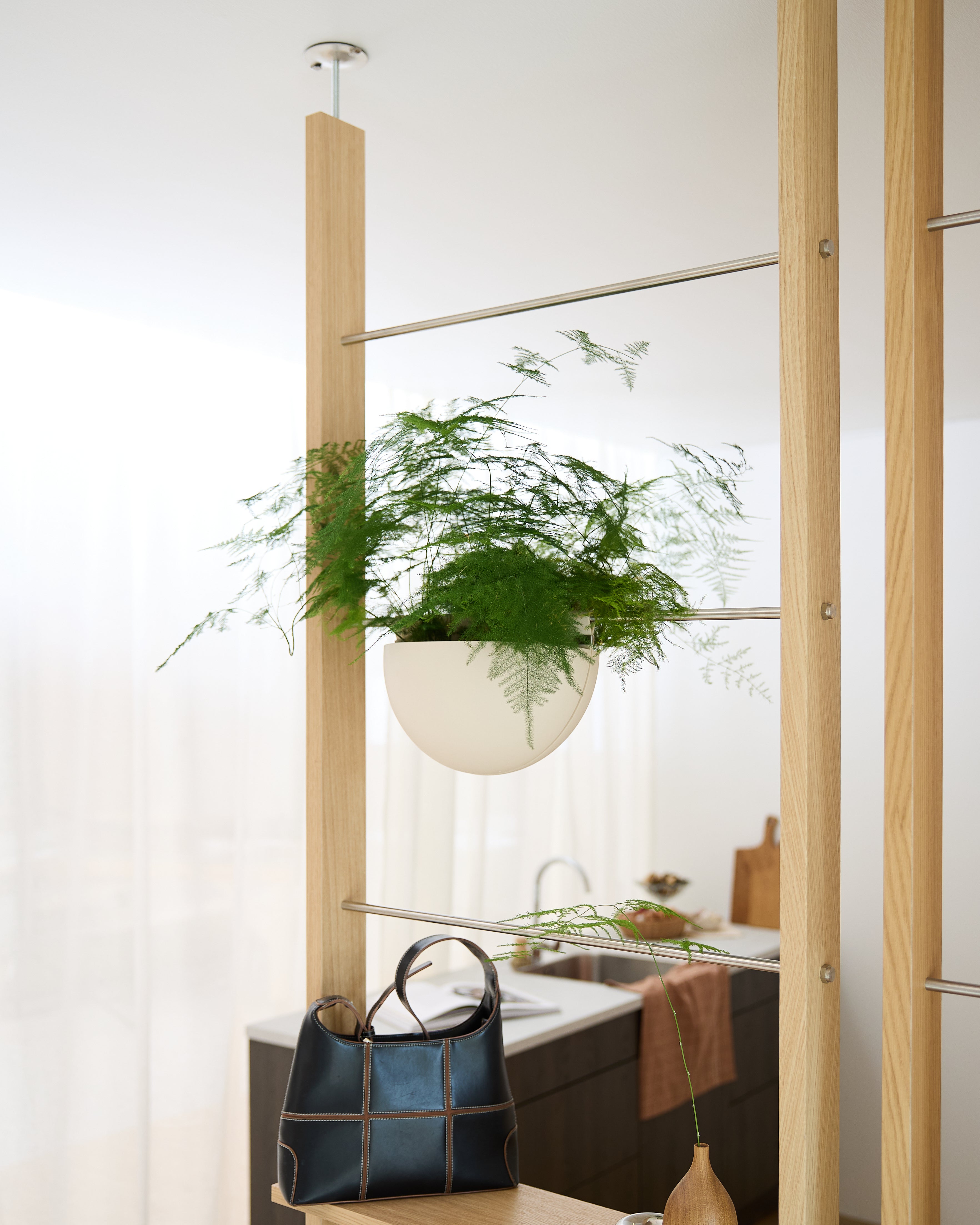 Un Gro Soft Pocket (4 L) de la marque WoodUpp est fixé sur un cadre en bois au-dessus dun sac à main noir, dans une cuisine lumineuse et moderne.