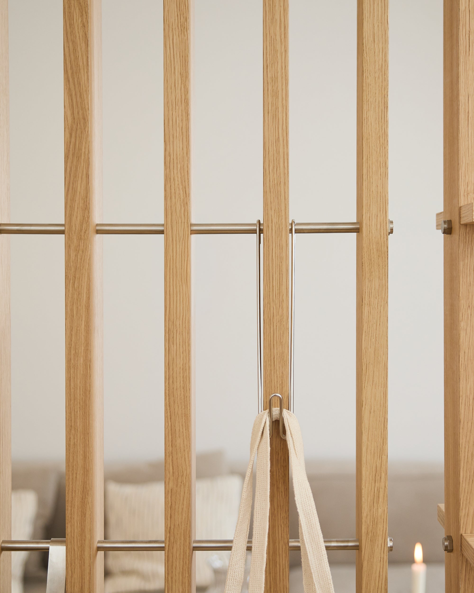 Portail en bois clair avec des barreaux métalliques, un ruban beige et trois crochets WoodUpp Alva Wire Hooks/BM1 ; canapé et bougie flous en arrière-plan.