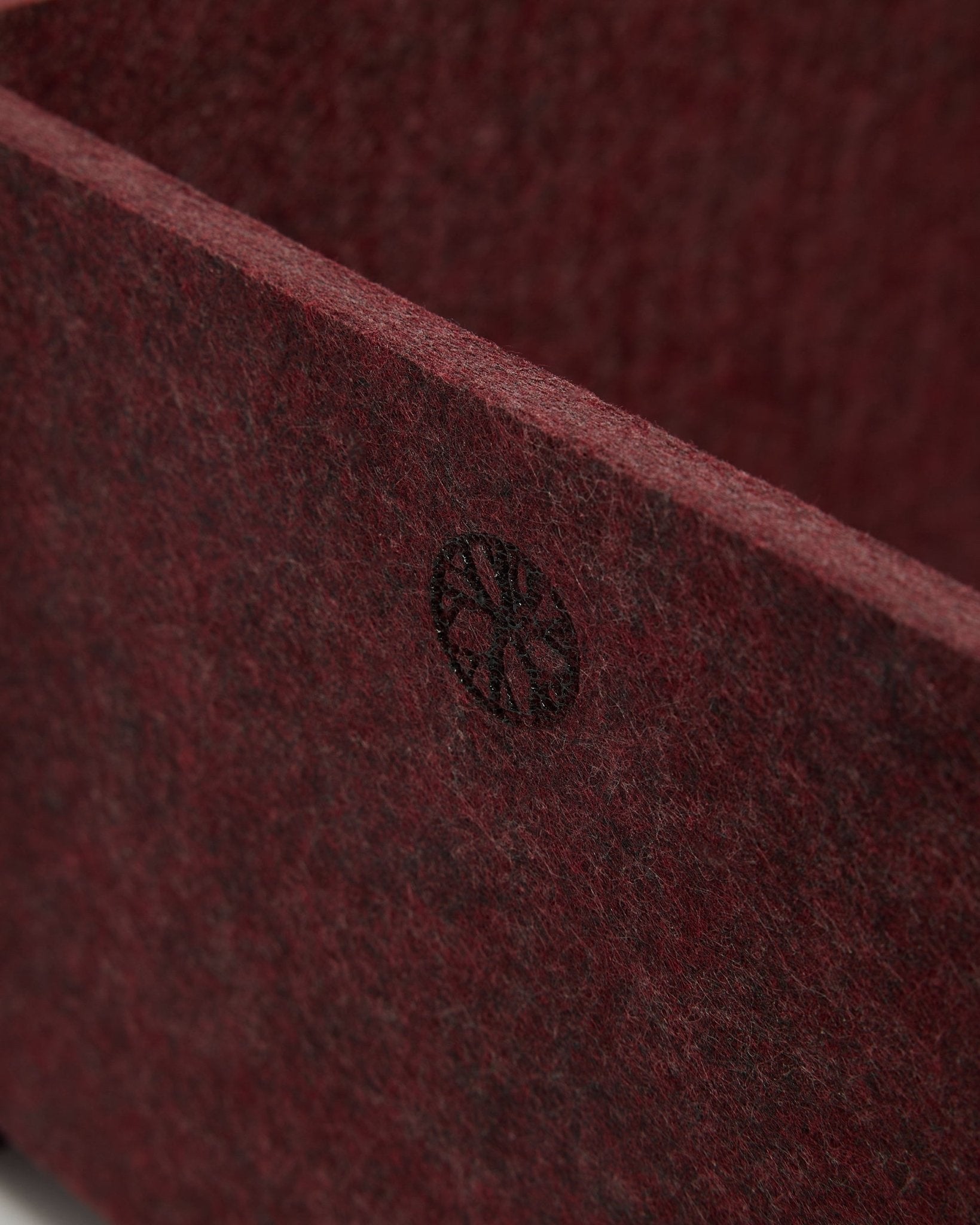 Gros plan sur WoodUpp Vigg | Felt Box / BM2 en ox red, montrant le feutre PET texturé et un emblème circulaire black dans le coin. Design d’accessoire acoustique nordique.