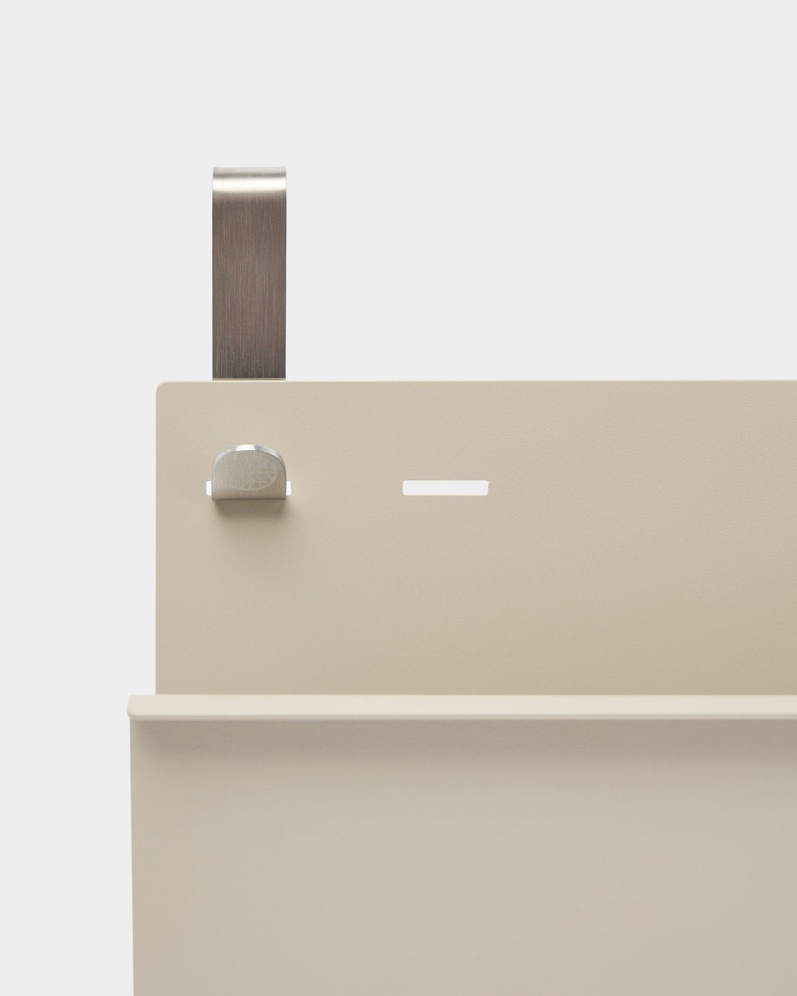 Gros plan sur le porte-revues Nell de WoodUpp en beige, en steel thermolaqué, avec tablette, fente, boulon et poignée courbe ; il fait office de séparateur de pièce ou de porte-revues.
