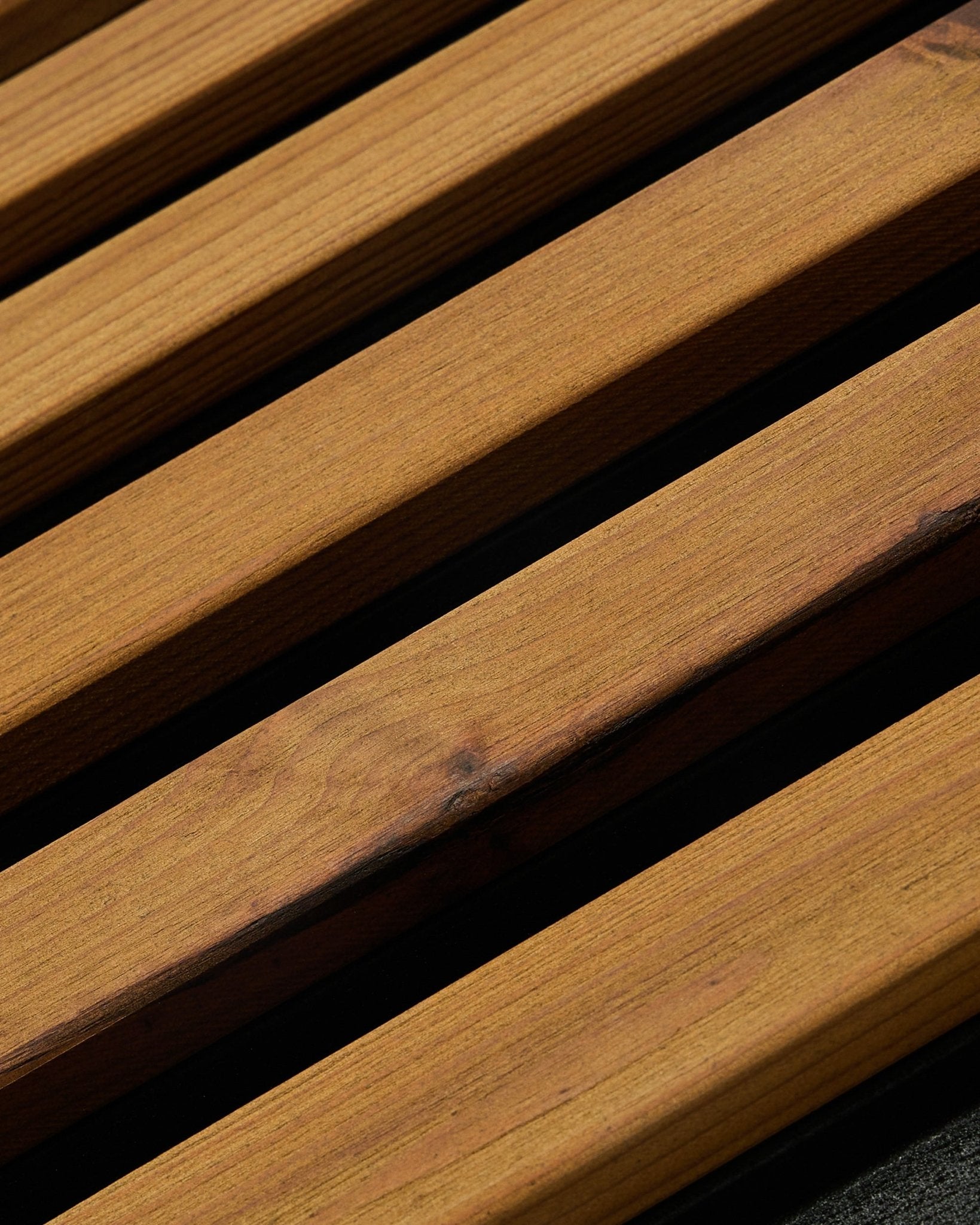 Gros plan sur un panneau de façade WoodUpp Aluwood en brown huilé (240 x 45,1 cm), en épicéa nordique traité thermiquement, présenté en angle pour montrer les lattes et les espaces foncés entre elles.