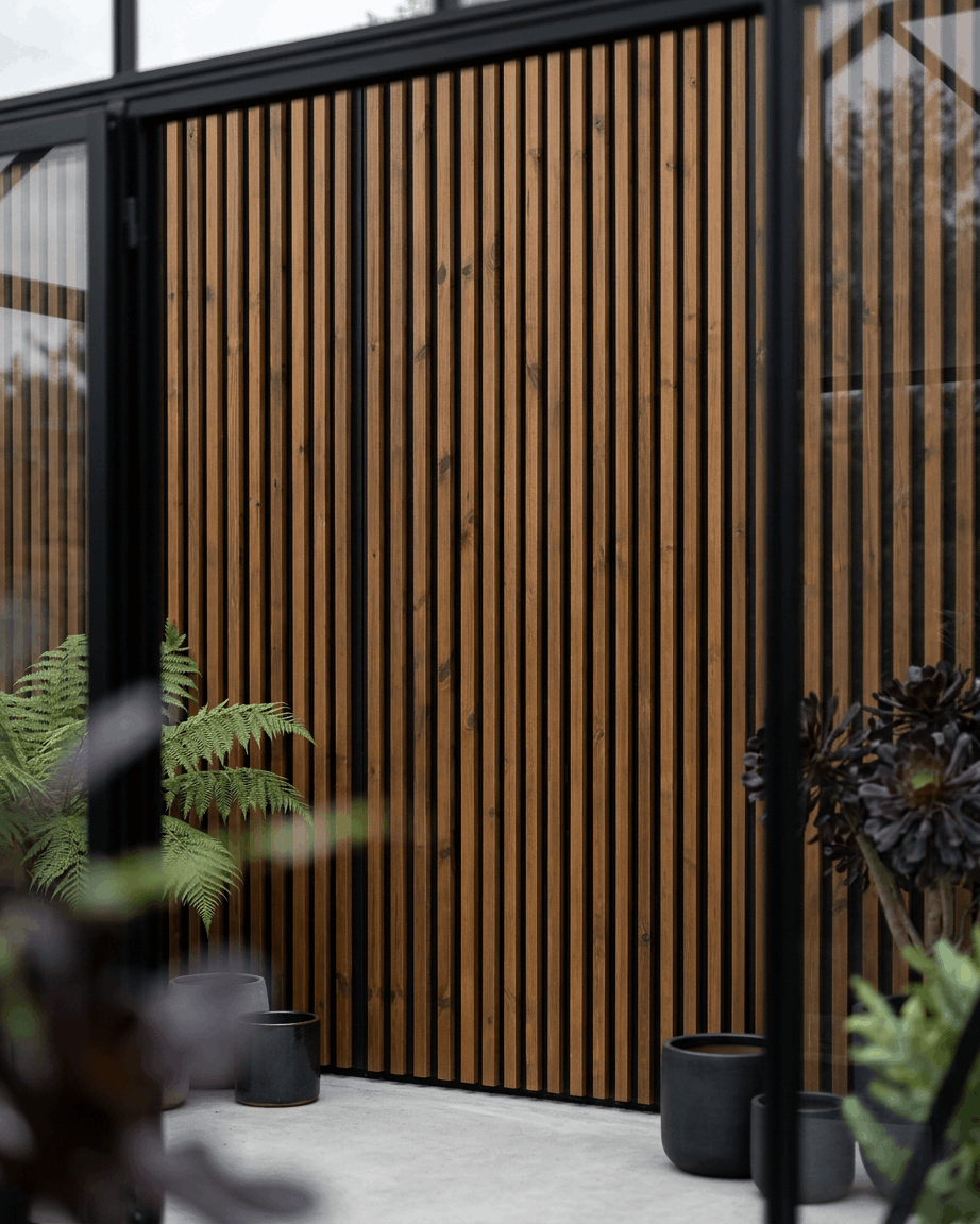 Panneau de façade extérieur WoodUpp Aluwood huilé brown, associé à des jardinières black et des plantes vertes, pour créer un patio nordique minimaliste.