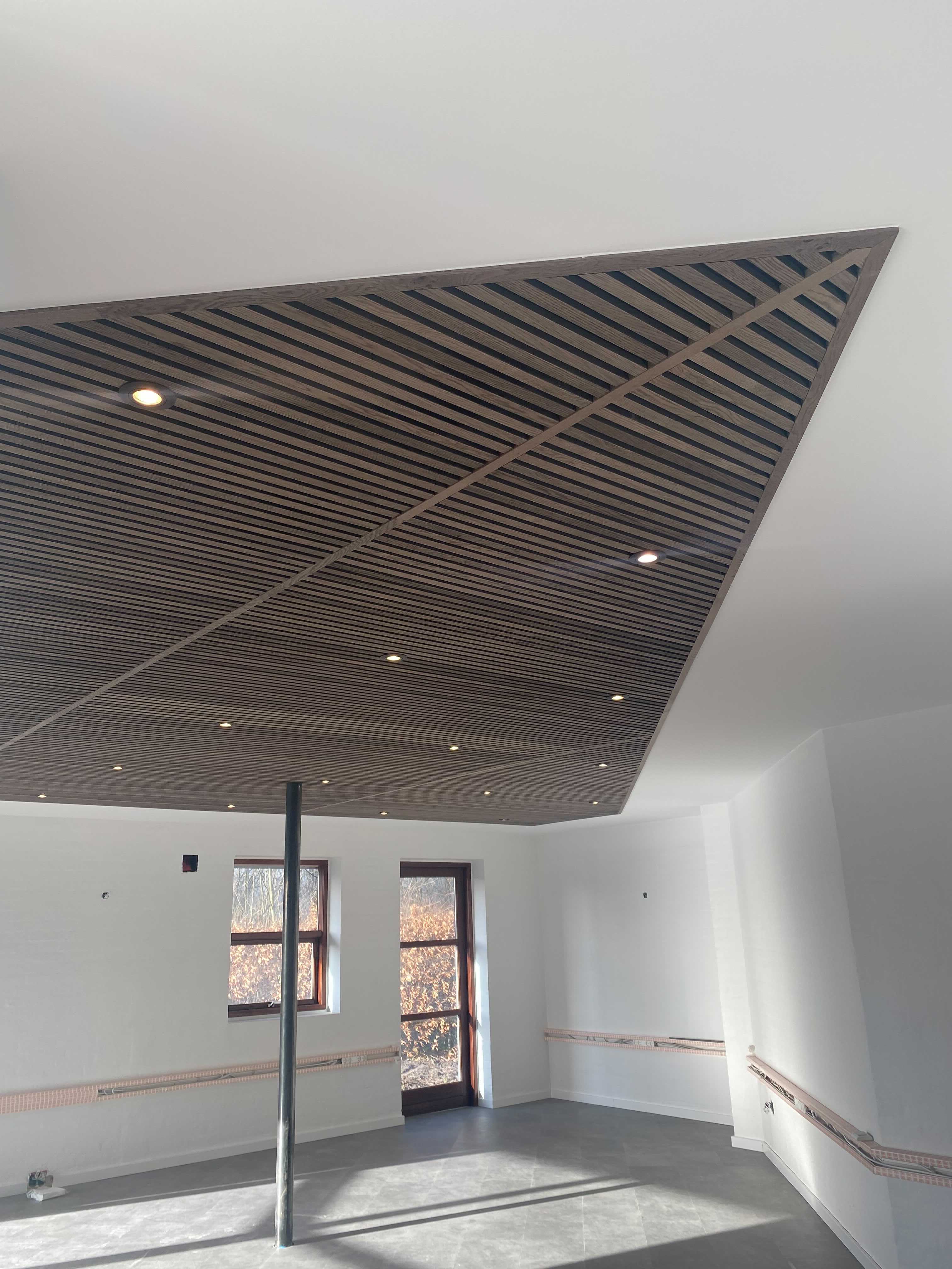Modern room with slanted Akupanel acoustic wood panel ceiling, recessed lighting, white walls, large window, and a metal support pole.