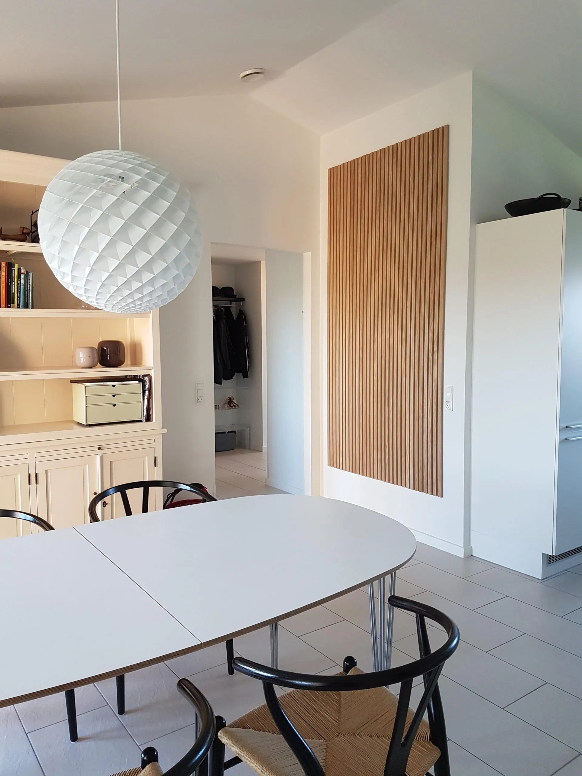 Salle à manger moderne avec une table ovale blanche, des chaises noires, une grande lampe suspendue texturée et des armoires acoustiques Akupanel en bois clair.