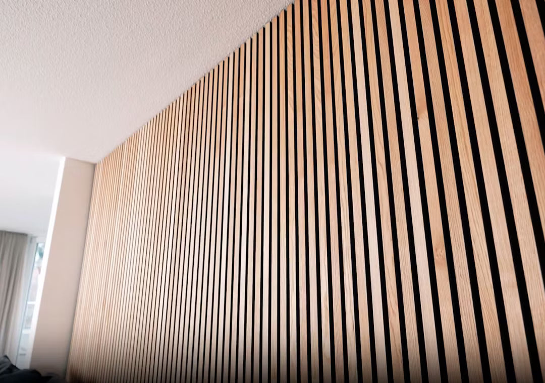 Gros plan du panneau acoustique en bois Akupanel, composé de lames verticales en bois à motif rayé, installé sur un mur intérieur sous un plafond blanc.