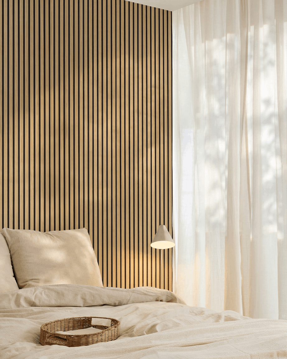 Chambre minimaliste avec linge de lit beige, un mur d’accent en Panneau acoustique Southern Oak WoodUpp Akupanel, un plateau tressé sur le lit et des rideaux voilages laissant entrer la lumière naturelle.