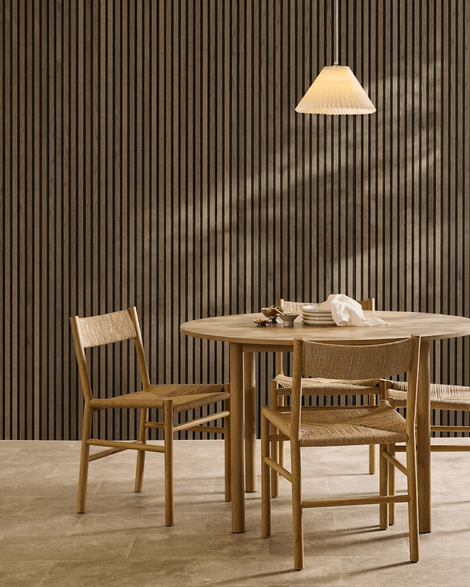Salle à manger minimaliste avec table ronde, chaises tressées et suspension, mettant en valeur un panneau acoustique à lattes WoodUpp Akupanel Rustic Grey Oak.