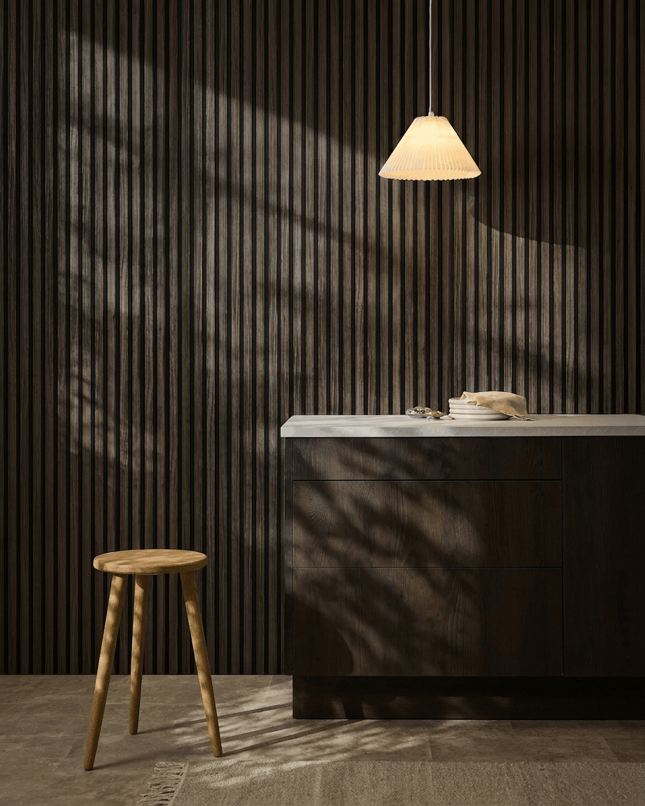 Cuisine minimaliste avec les panneaux acoustiques muraux WoodUpp Akupanel Black Oak, un tabouret en bois, un plan de travail blanc, une suspension beige et des ombres baignées de soleil.