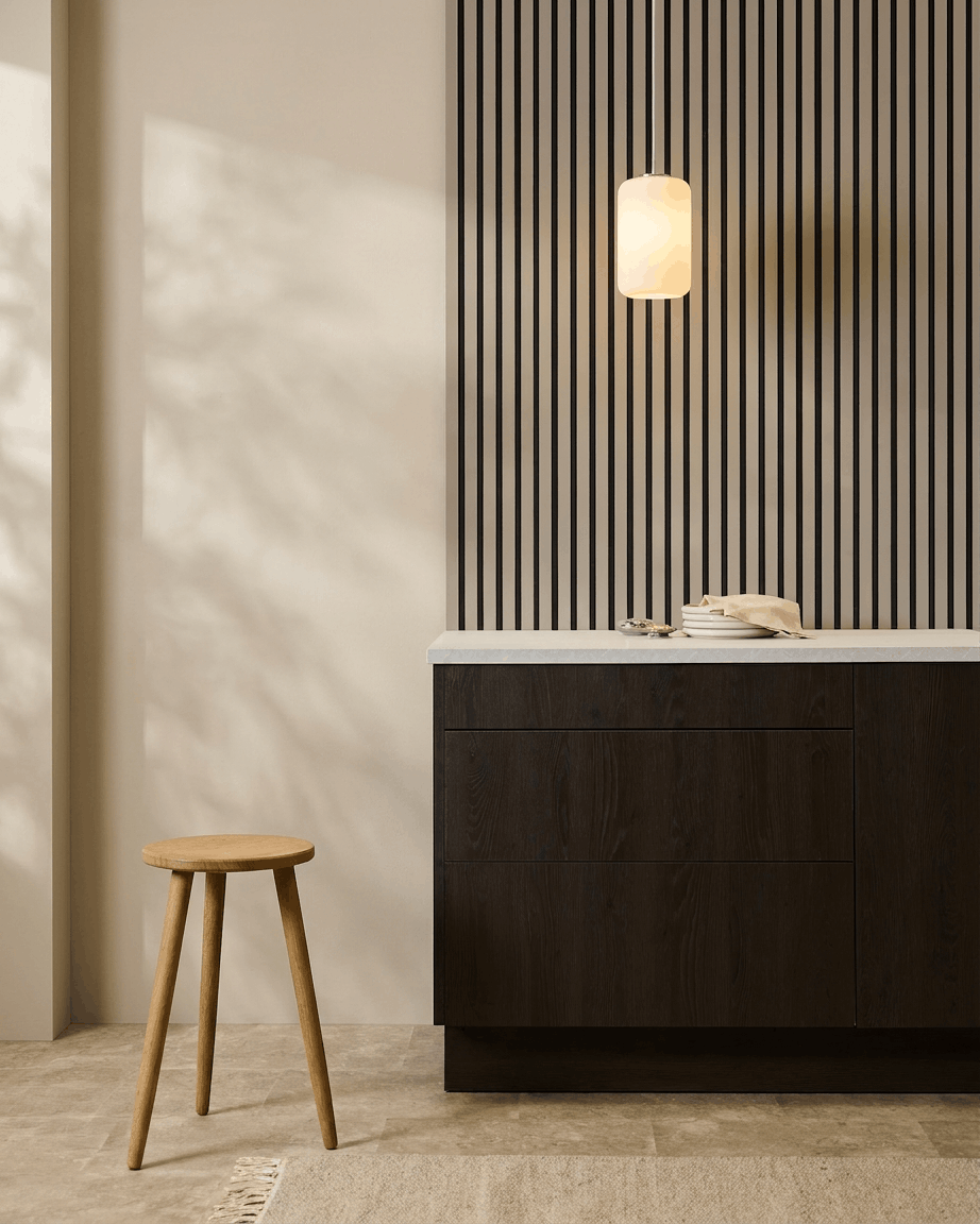 Cuisine minimaliste avec des panneaux acoustiques WoodUpp Akupanel (Stone, Black Felt) sur le mur, un tabouret en bois, des placards foncés et une suspension dans des tons neutres.