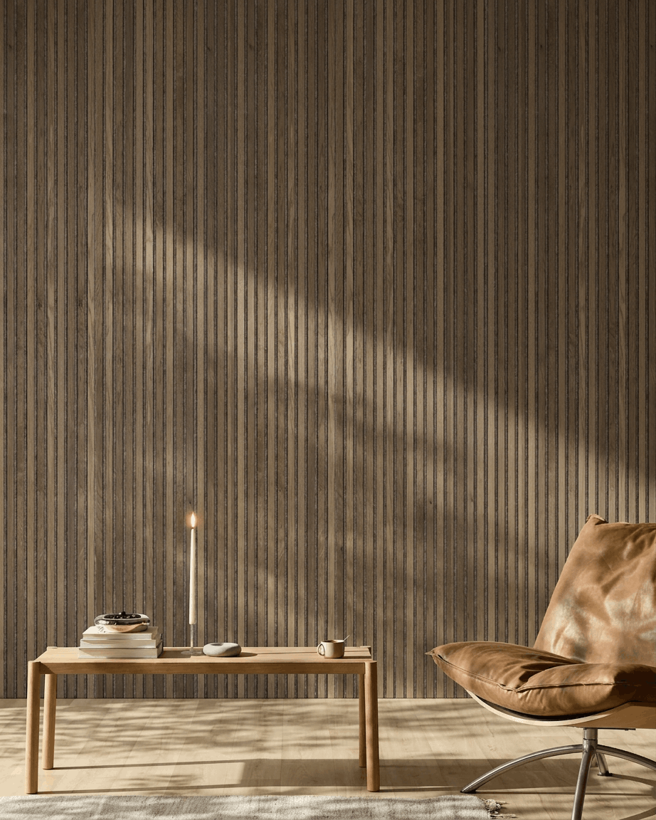 Une pièce moderne avec un fauteuil en cuir brown, une table en bois et un panneau WoodUpp Akupanel en Rustic Grey Oak monté au mur, baigné d’une lumière douce du soleil.