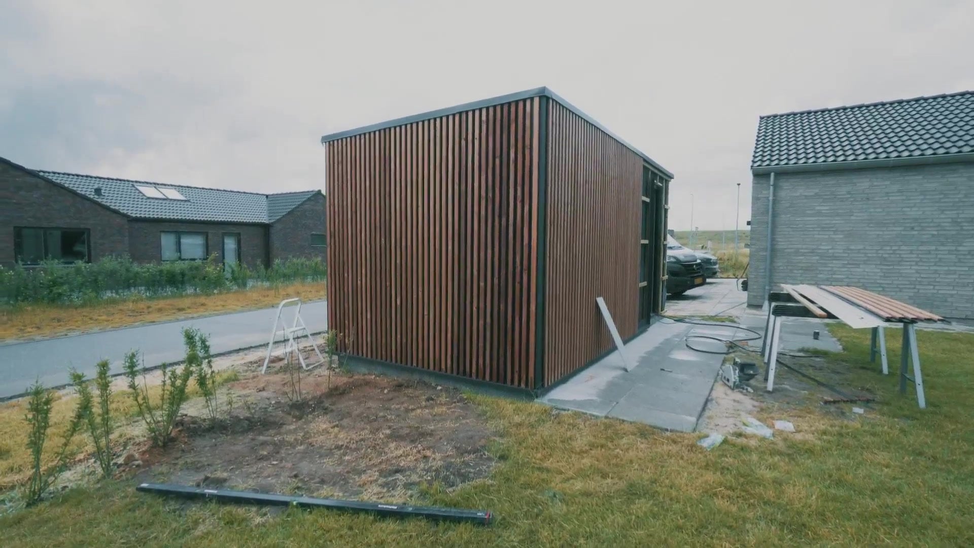 Finished garden shed clad in vertical brown Aluwood slats with a black roof edge, in a residential area