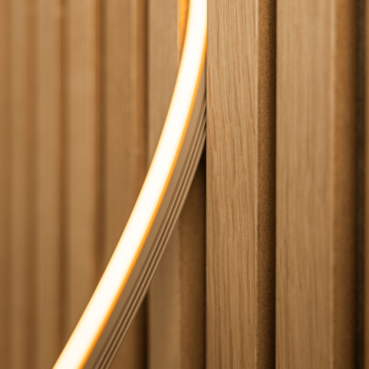 Gros plan sur la bande lumineuse LED WoodUpp Lumi en beige (240 cm), diffusant une lumière jaune chaude sur les lattes en bois acoustiques Akupanel vertical ; compatible Philips Hue.