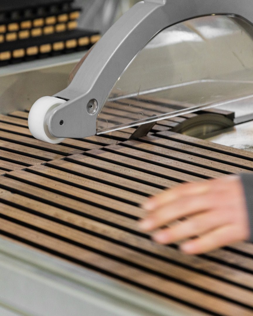 Une main utilise le Cutting service de précision WoodUpp pour découper des lattes Panneau acoustique régulièrement espacées, afin d’assurer un alignement précis lors de l’installation d’un mur en bois nordique.