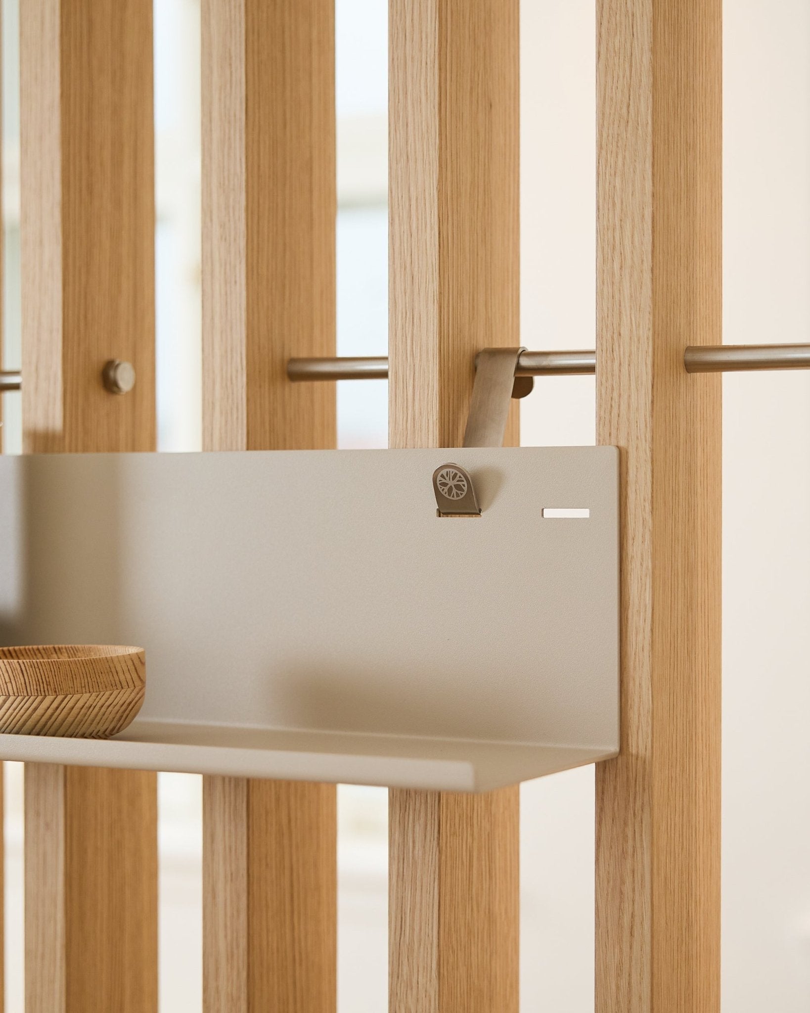 Étagère en métal WoodUpp Beige BM1 (63 x 13,4 cm) fixée sur un panneau acoustique à lattes vertical, avec un bol en bois sur le côté gauche de l’étagère.