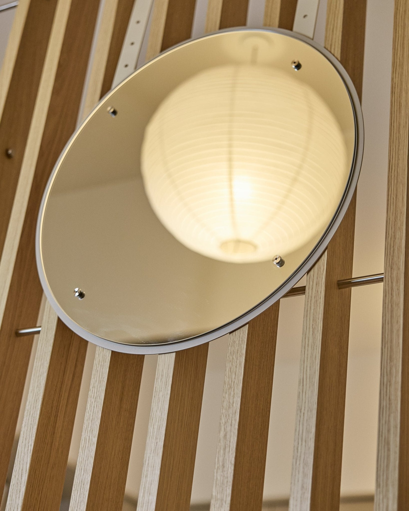 Le Vala | Mirror / BM1, D54 cm de WoodUpp est un miroir rond réglable en hauteur, monté sur des panneaux muraux acoustiques à lattes vertical, qui reflète une lanterne en papier lumineuse.