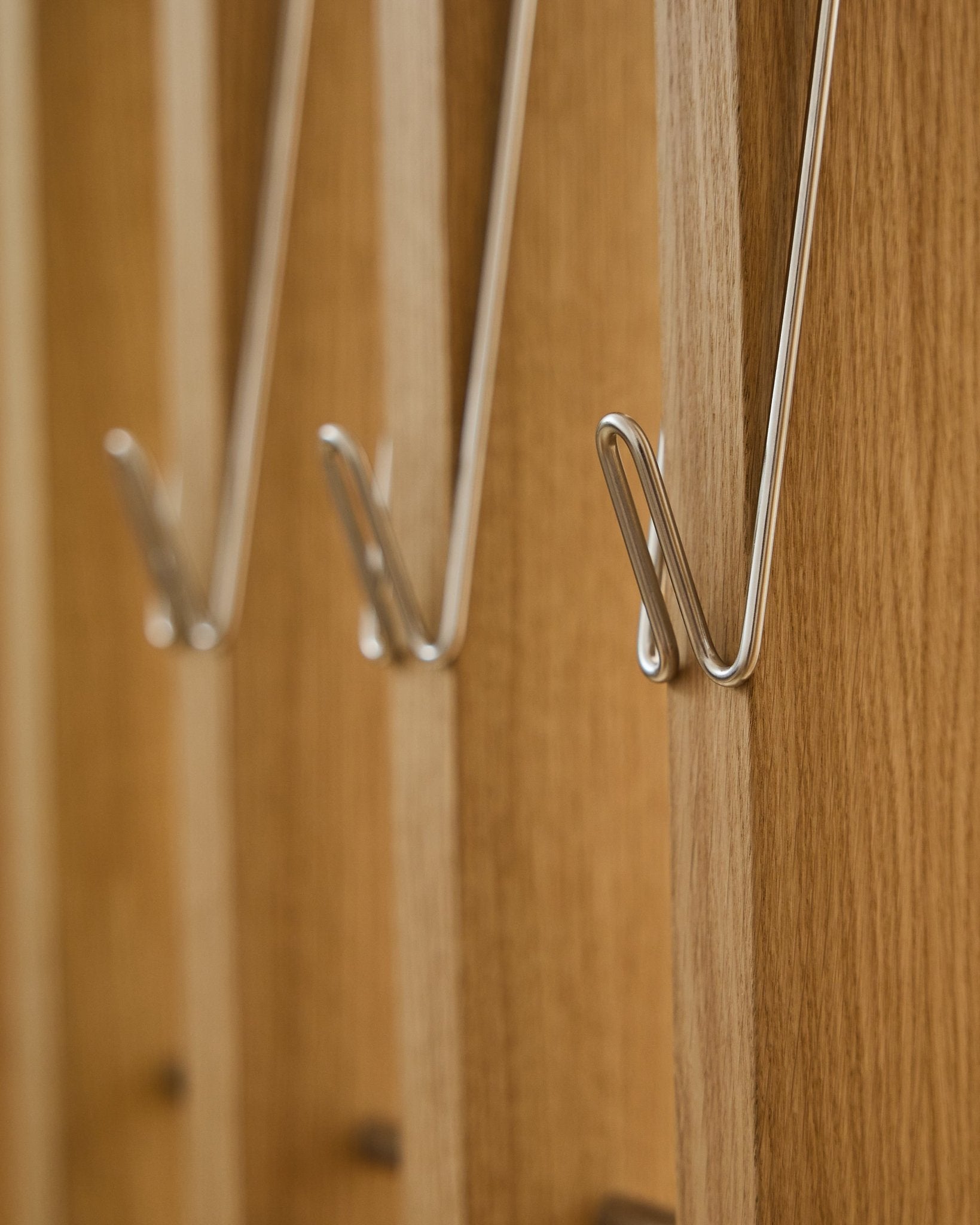 Gros plan sur trois Alva | Wire Hook / BM1, Stainless Steel, Long de WoodUpp, montés en rangée sur des panneaux acoustiques en bois Akupanel et projetant de douces ombres.